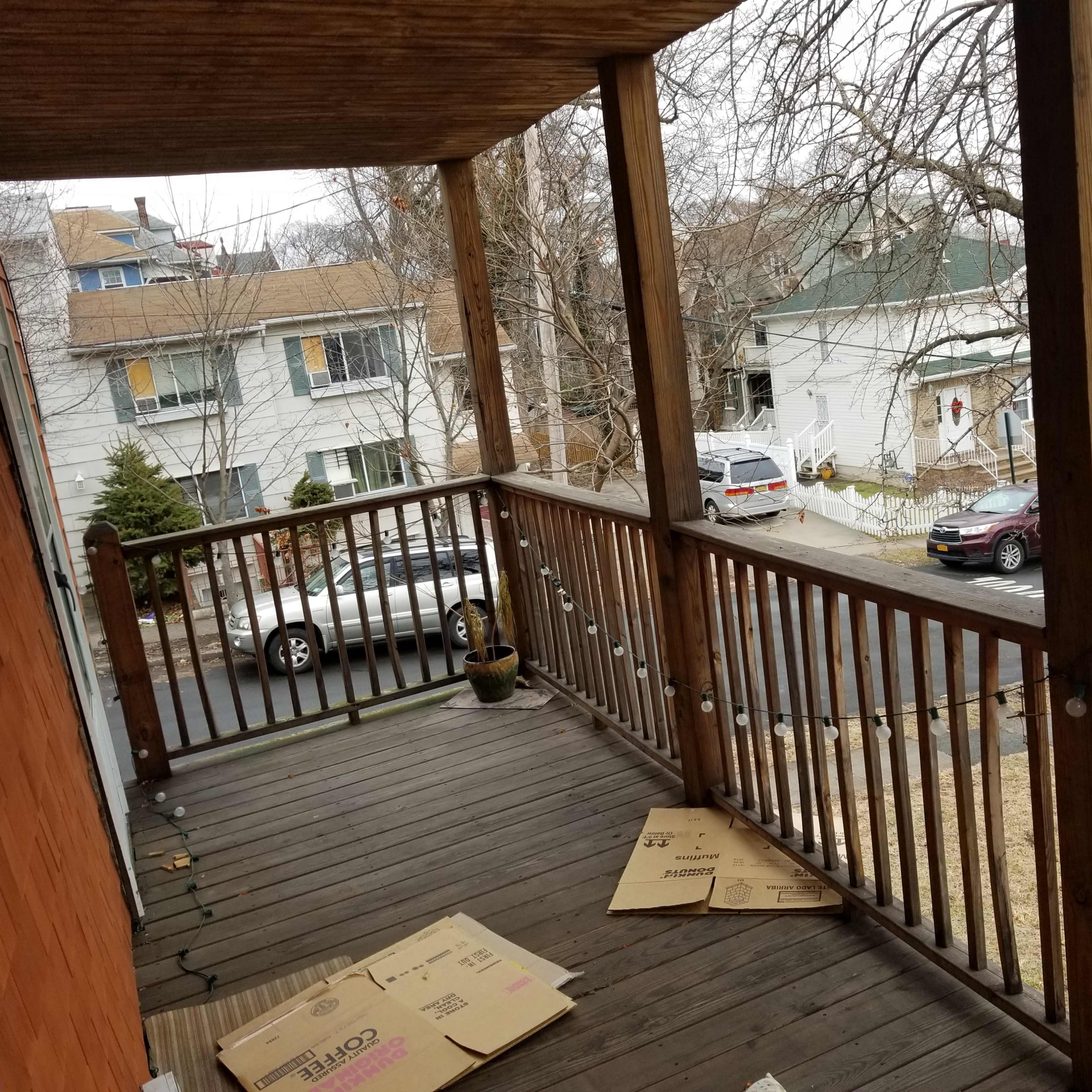 A wooden porch with several cardboard boxes on the floor and a view of nearby houses and parked cars.