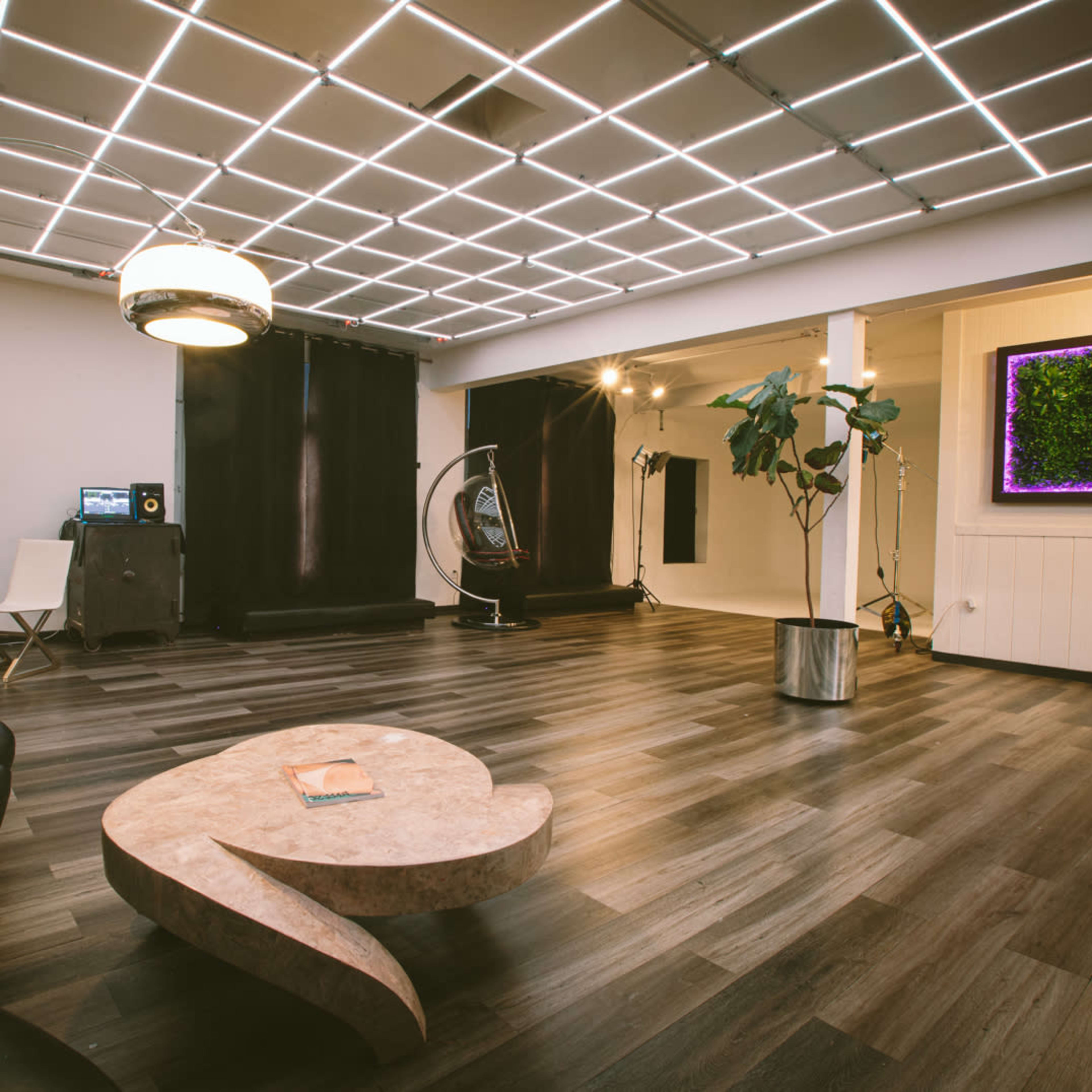 A spacious room with a modern design, featuring a curved marble coffee table, a black couch, and a wall-mounted screen displaying greenery.