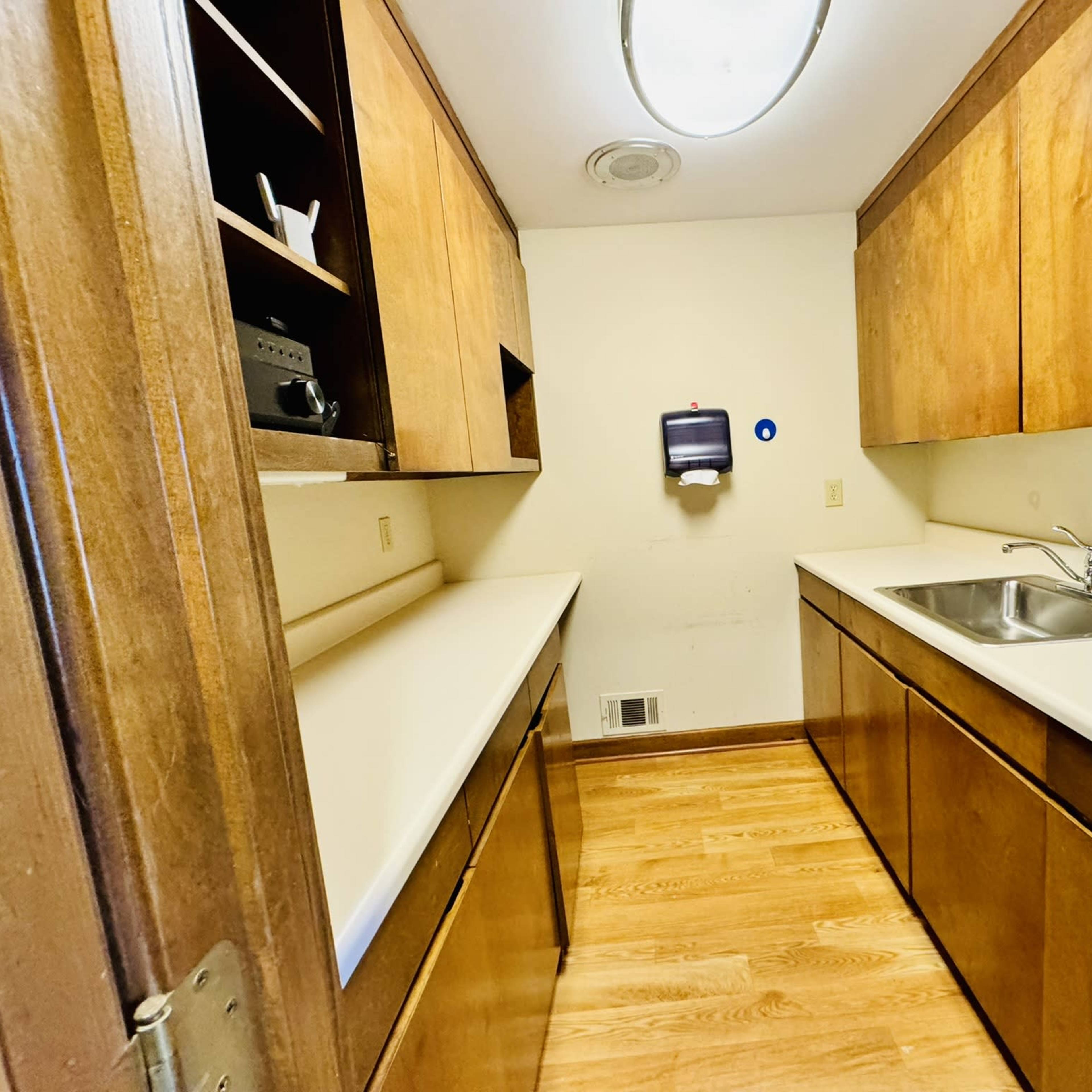 A small laundry room with wooden cabinets, a sink, and a white countertop.