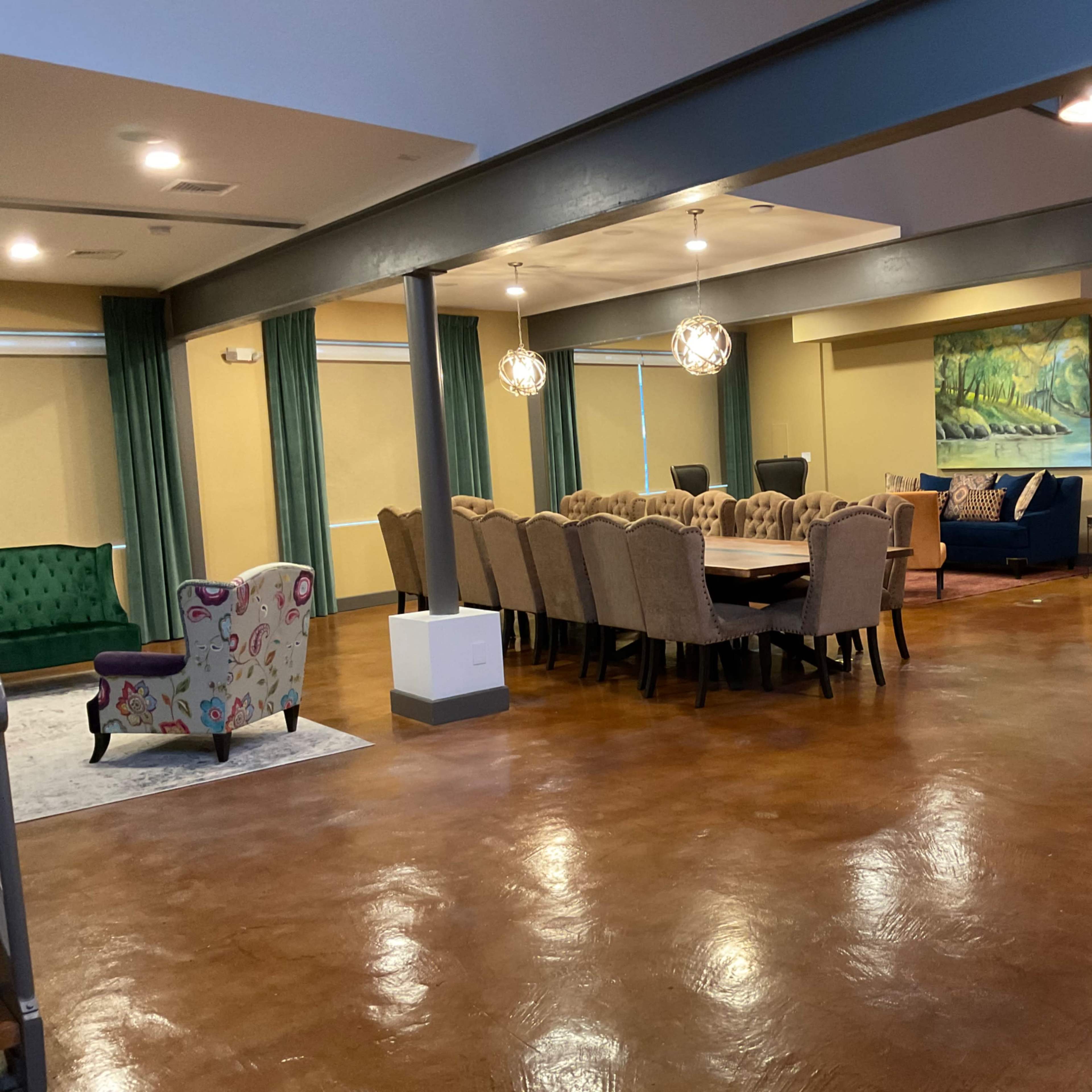 A spacious room with a large dining table surrounded by chairs, a seating area with a green sofa, and decorative lighting fixtures.