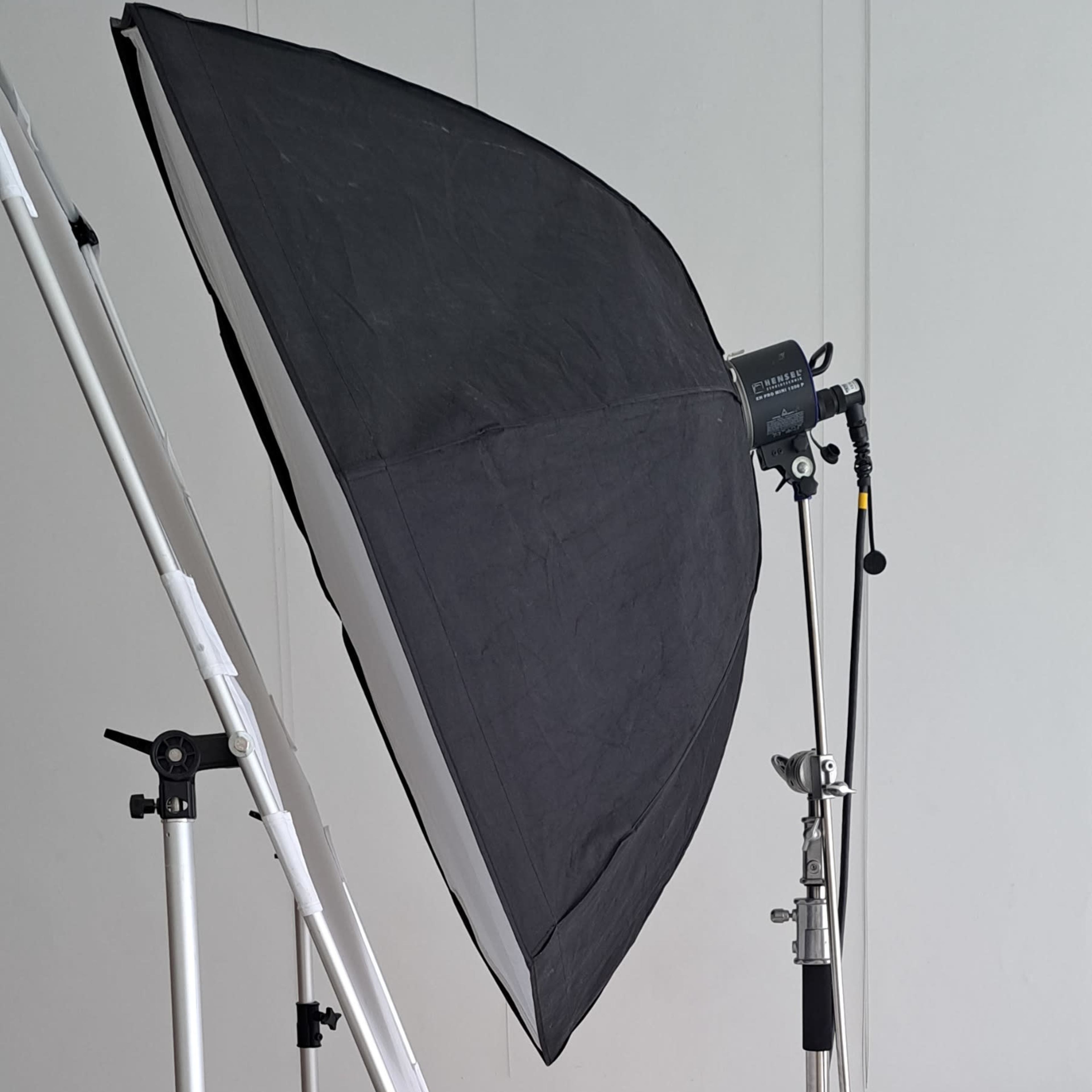A studio lighting setup with a softbox mounted on a stand, positioned in an empty room with a plain floor.