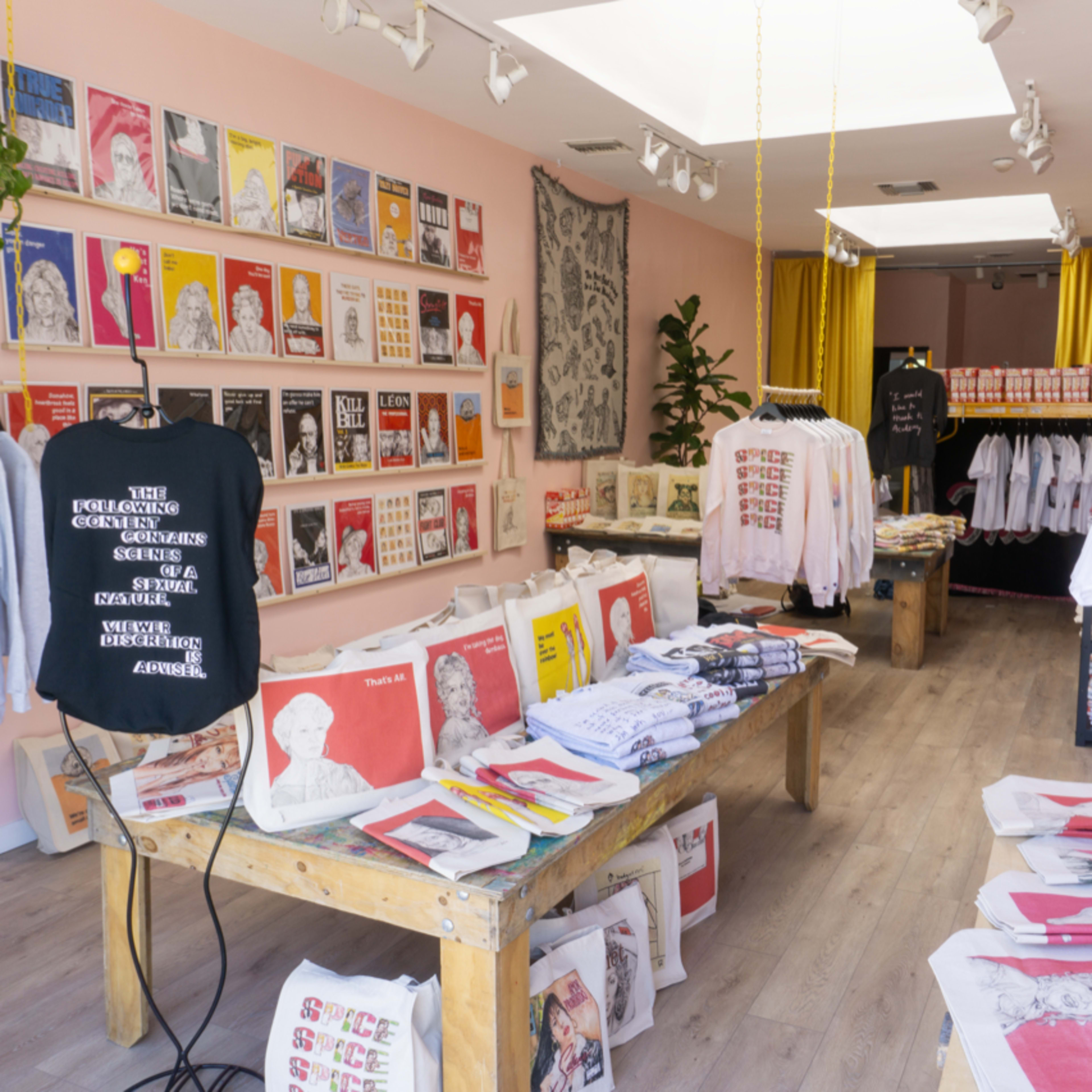 A colorful storefront featuring clothing and printed materials displayed on tables and hanging racks.