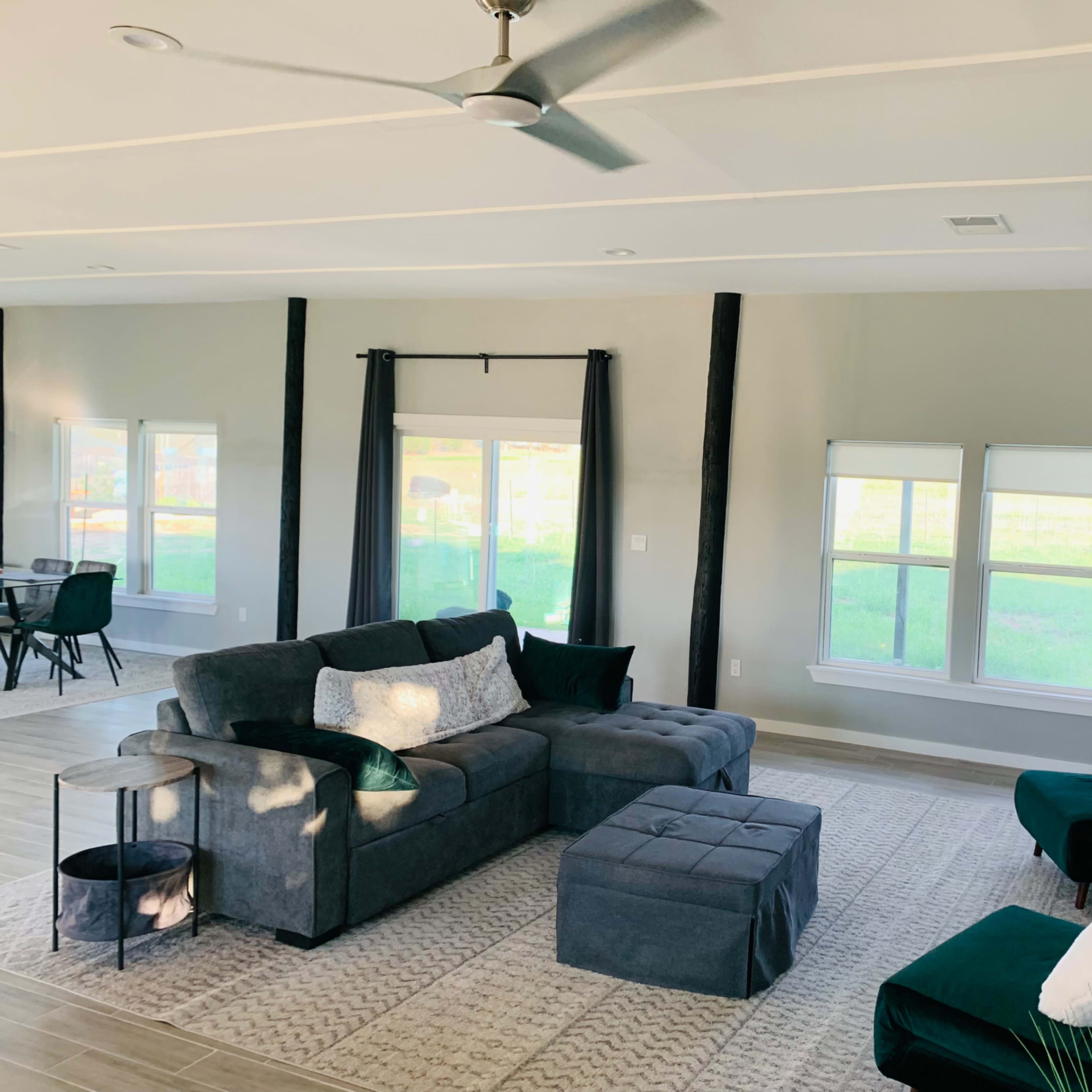 A modern living room featuring a gray sectional sofa, two armchairs, a small side table, and large windows letting in natural light.