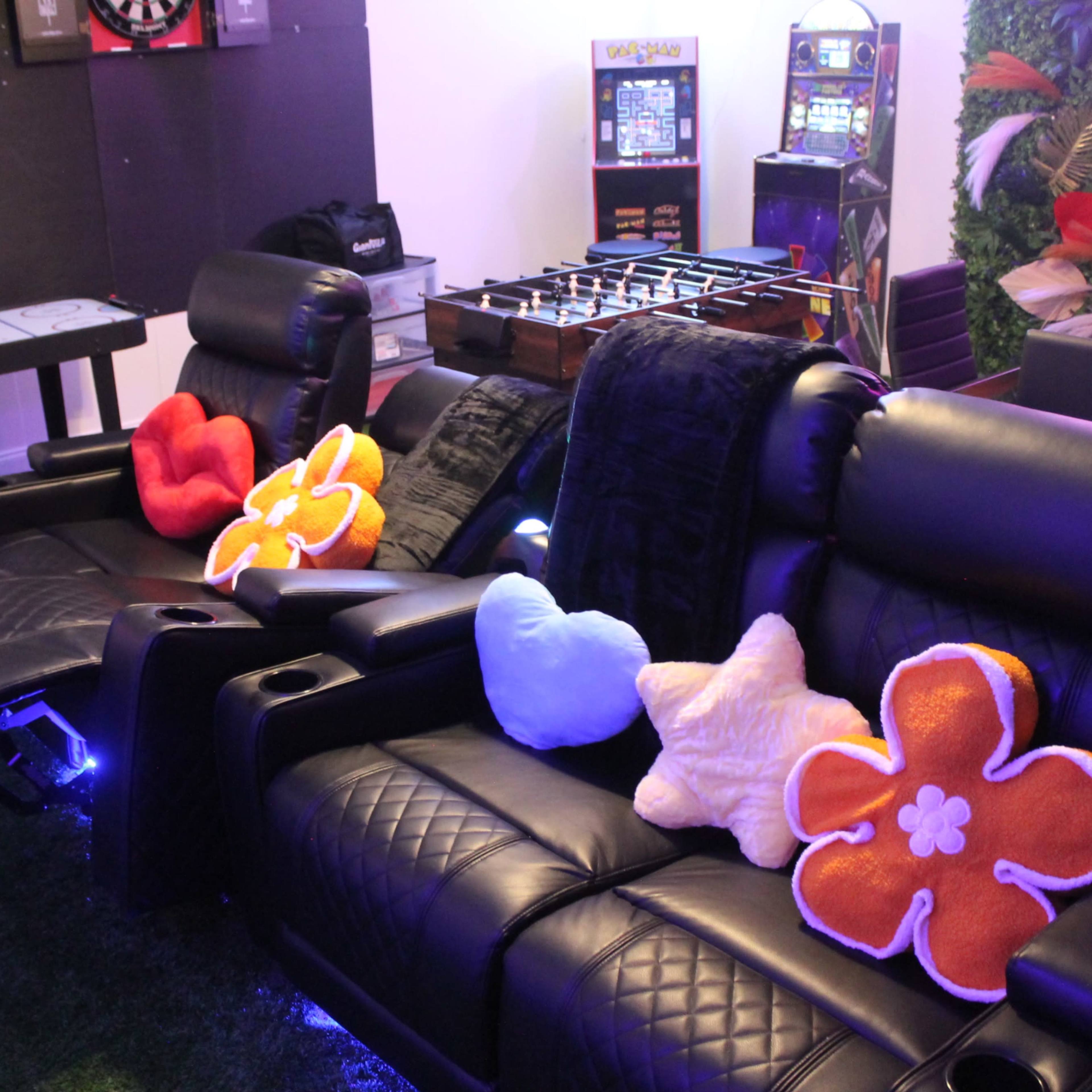 Black reclining chairs with colorful flower-shaped cushions in a game room featuring a dartboard and foosball table.
