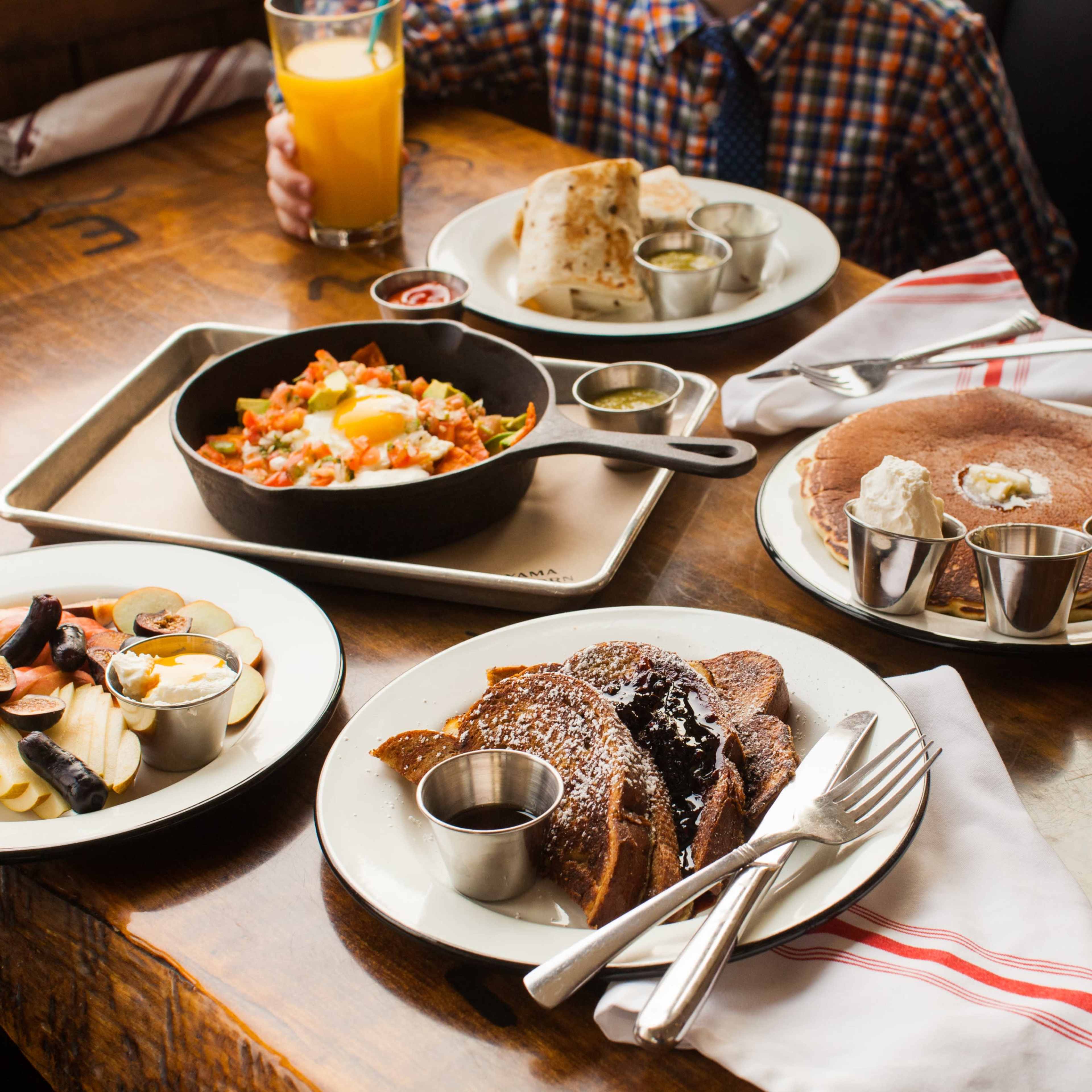 The table displays a variety of breakfast dishes, including French toast, a vegetable hash with an egg, and fruit sides, along with two glasses of orange juice.