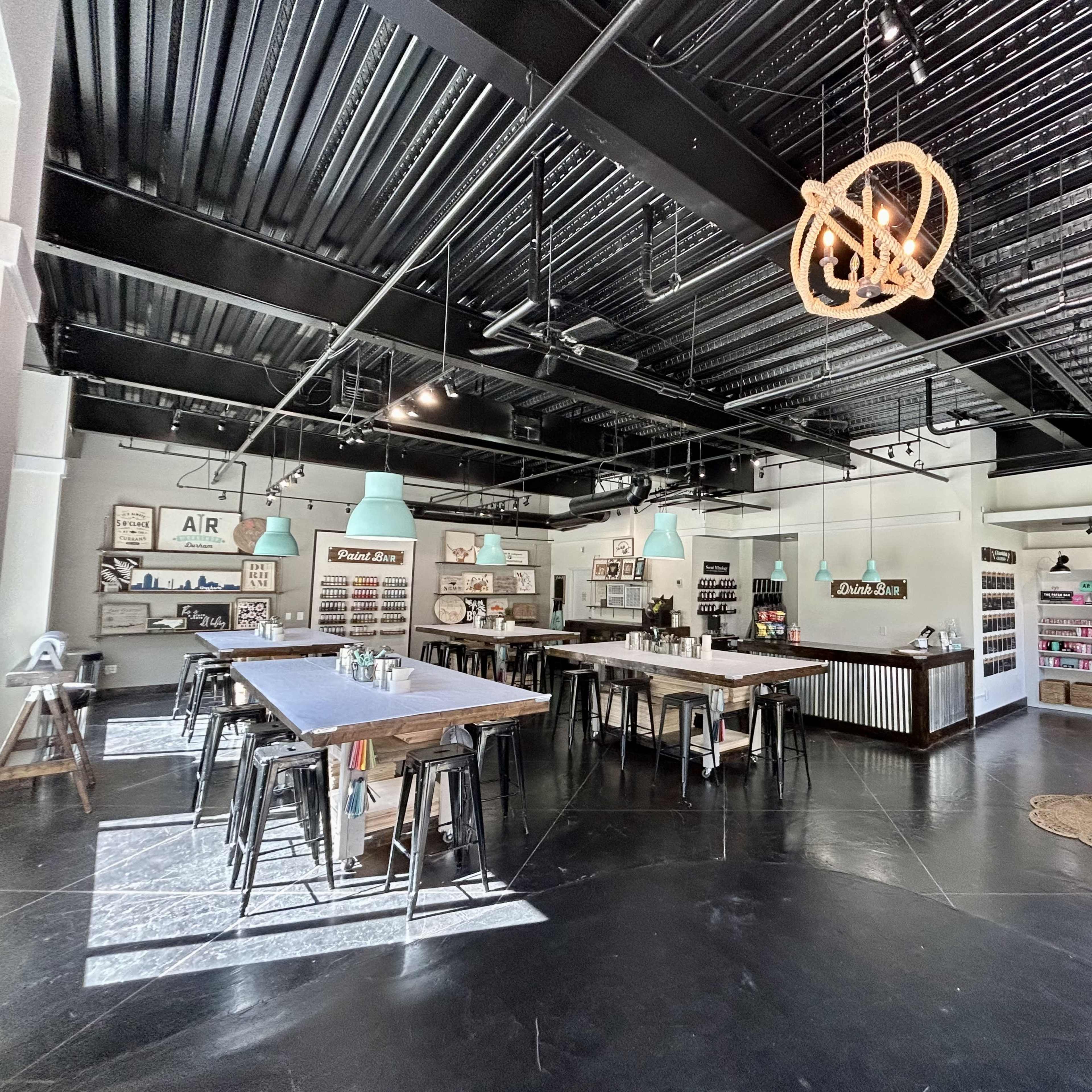 An interior of a modern retail space featuring wooden tables, metal stools, and shelves displaying various products.