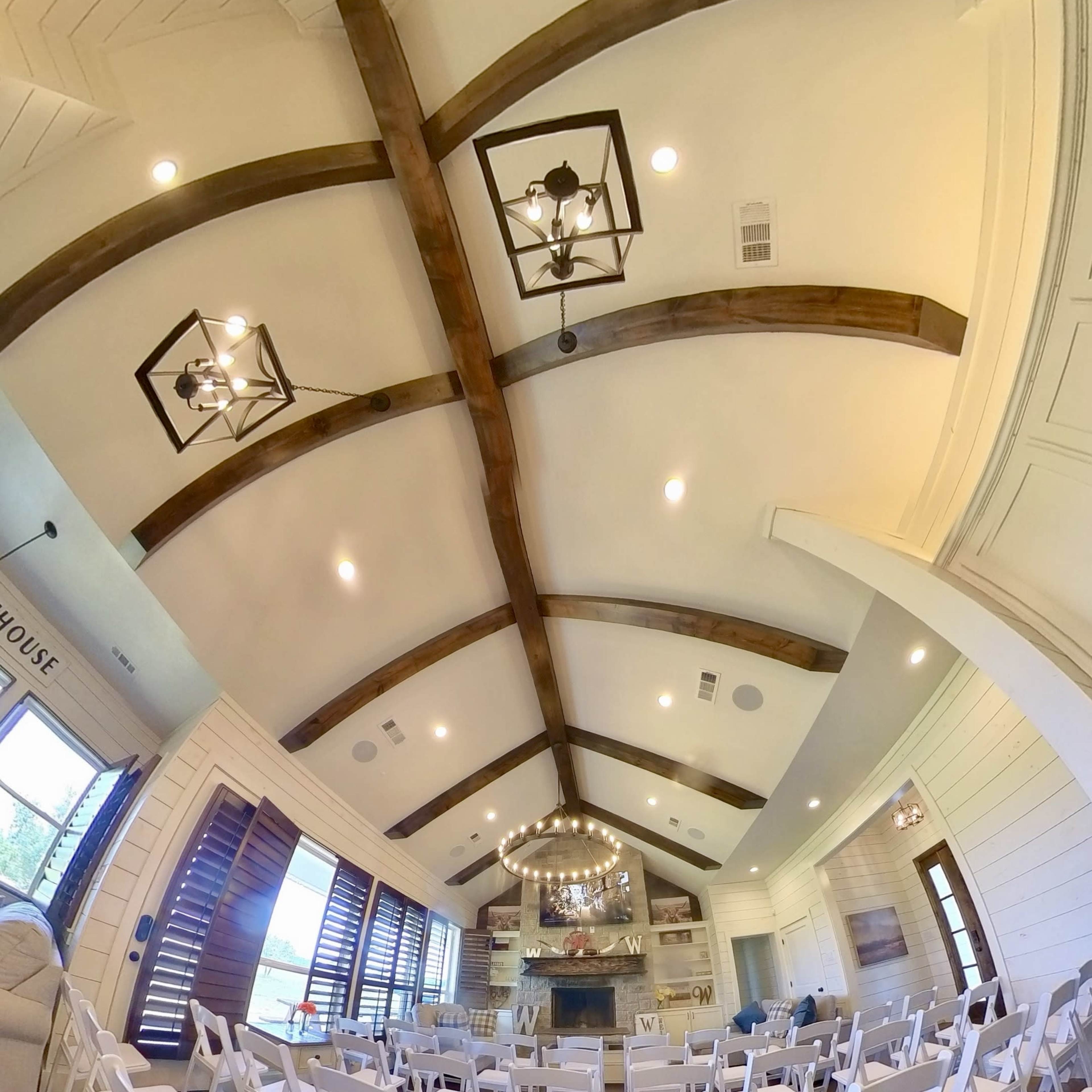 A spacious interior of a venue set up with white chairs arranged facing a central focal point, beneath exposed wooden beams and bright lighting.