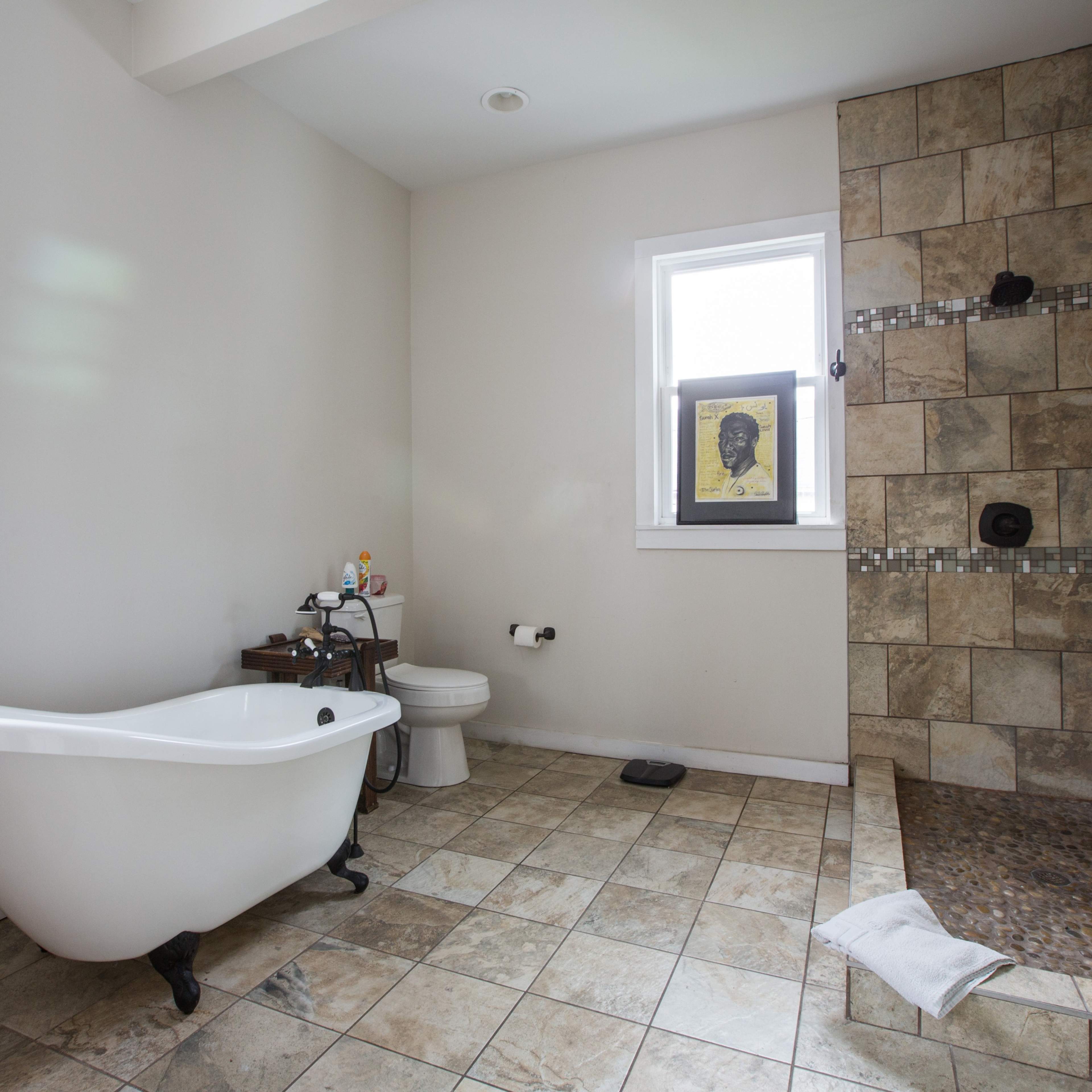 A bathroom featuring a freestanding white bathtub, a toilet, and a tiled walk-in shower area with a small frame hanging on the wall.