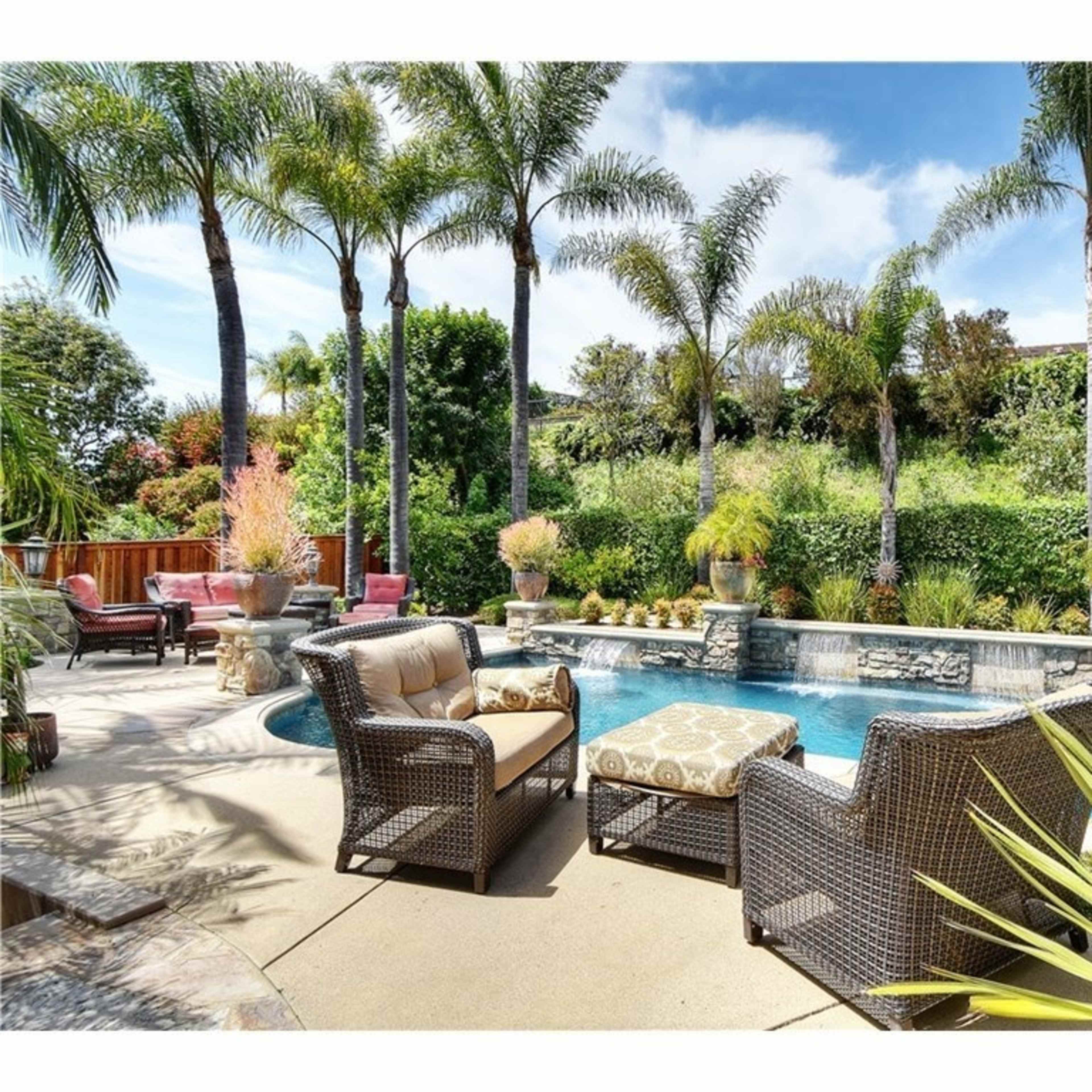 A backyard oasis featuring a swimming pool surrounded by palm trees, decorative plants, and outdoor seating.