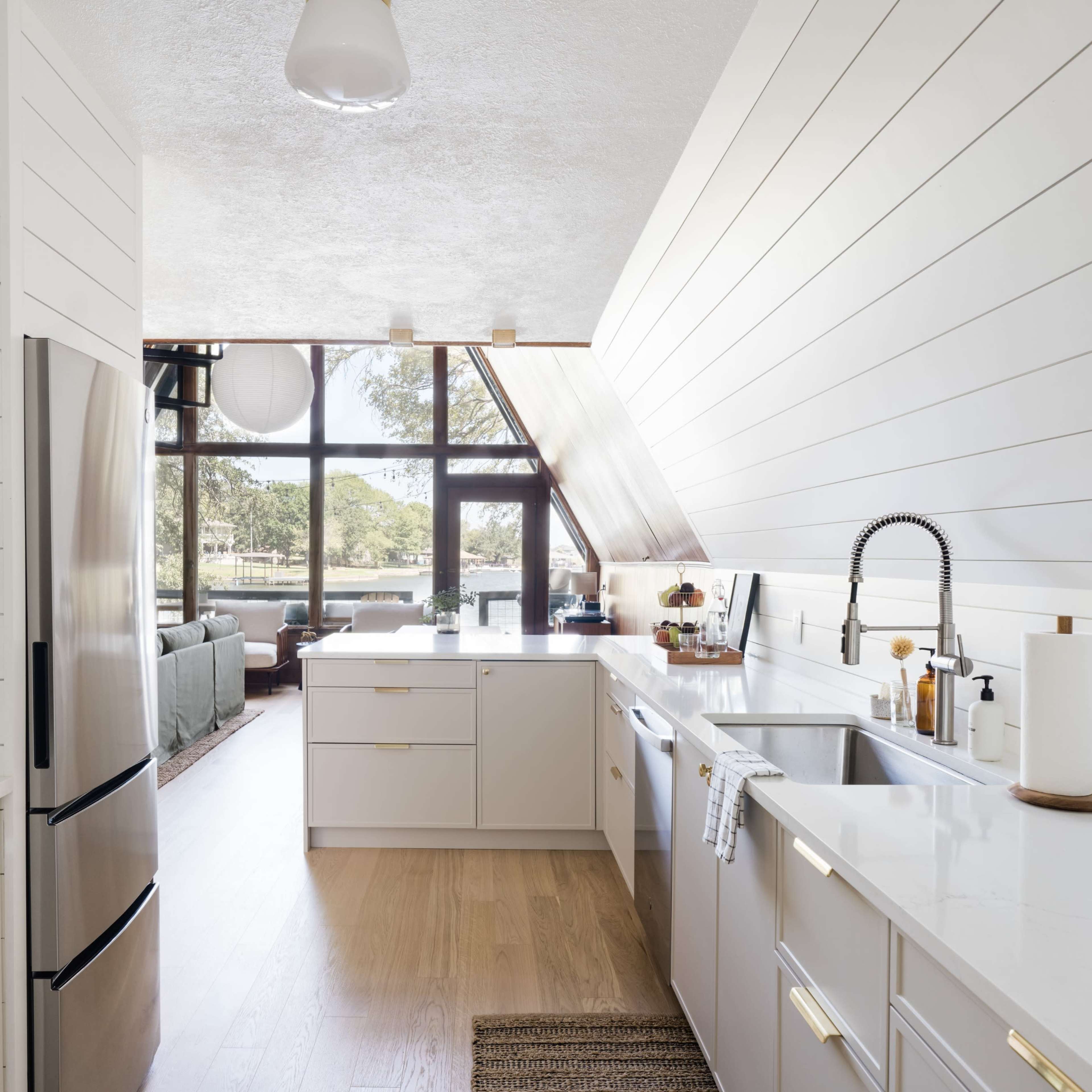 A modern kitchen with white cabinetry and a large window overlooking a living area.