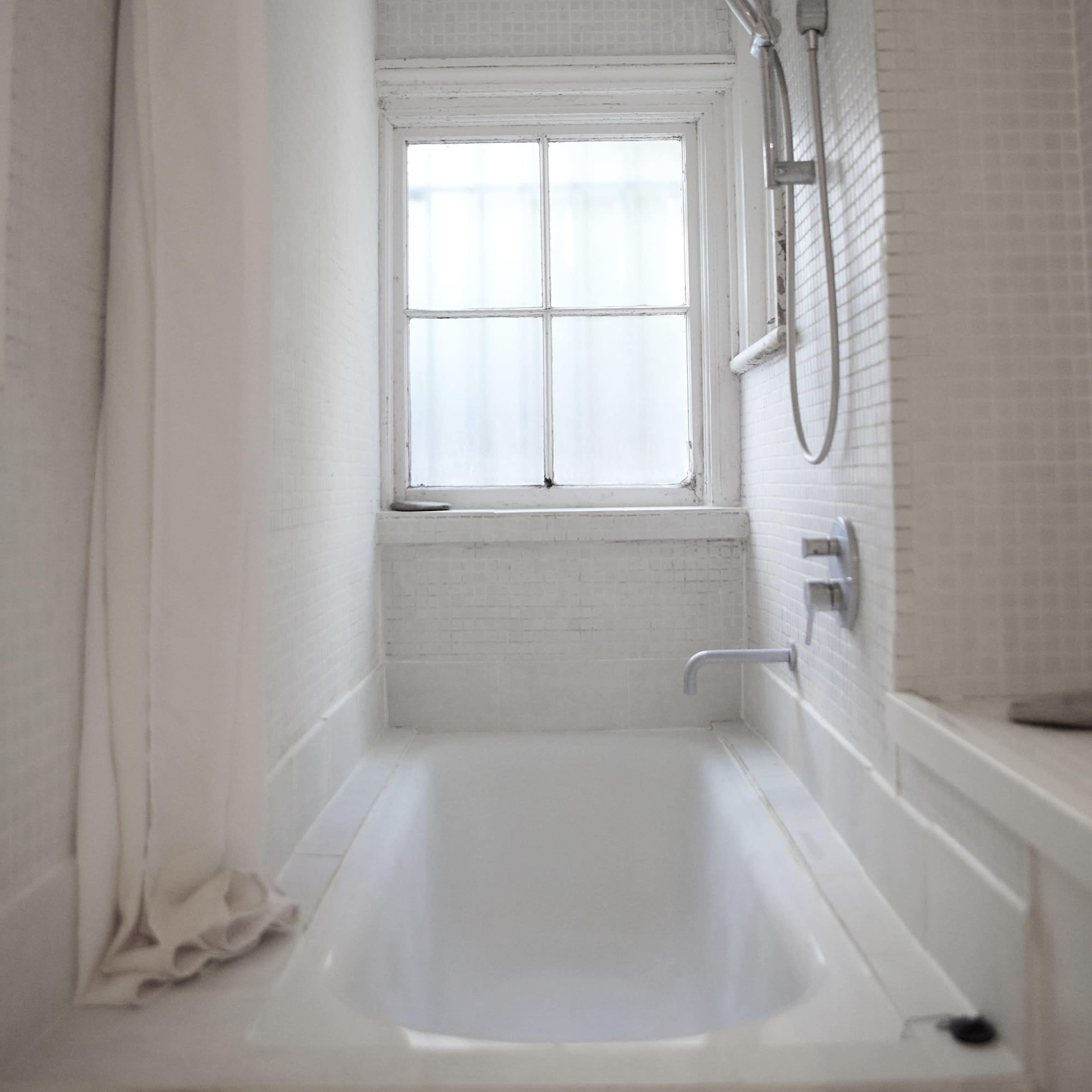 A bathroom with a white bathtub and a shower, featuring a window that lets in natural light.