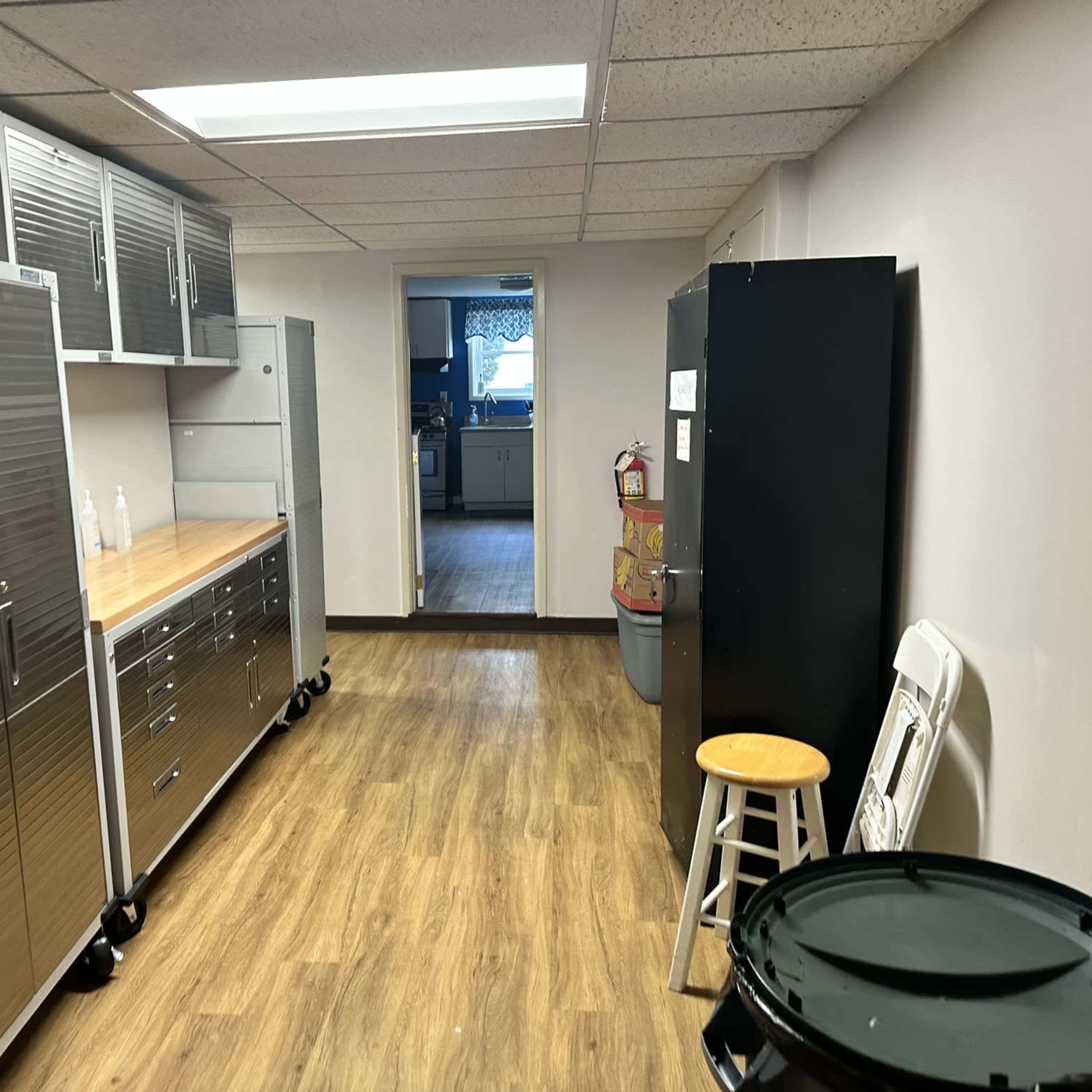 A narrow utility room featuring metallic cabinets on one side, a wooden countertop, and a doorway leading to another area.