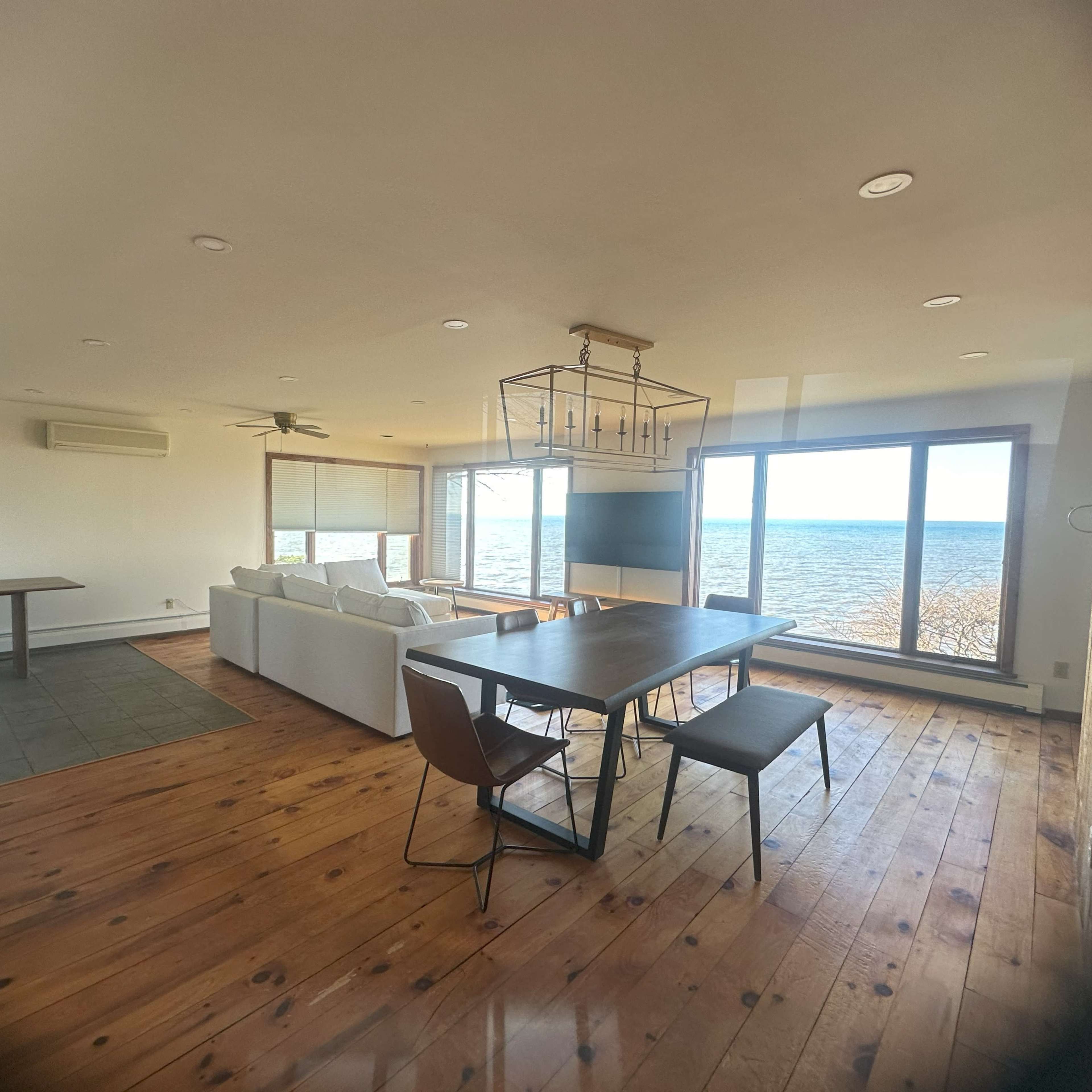 A stylish open-concept living and dining area with a large window overlooking a body of water.