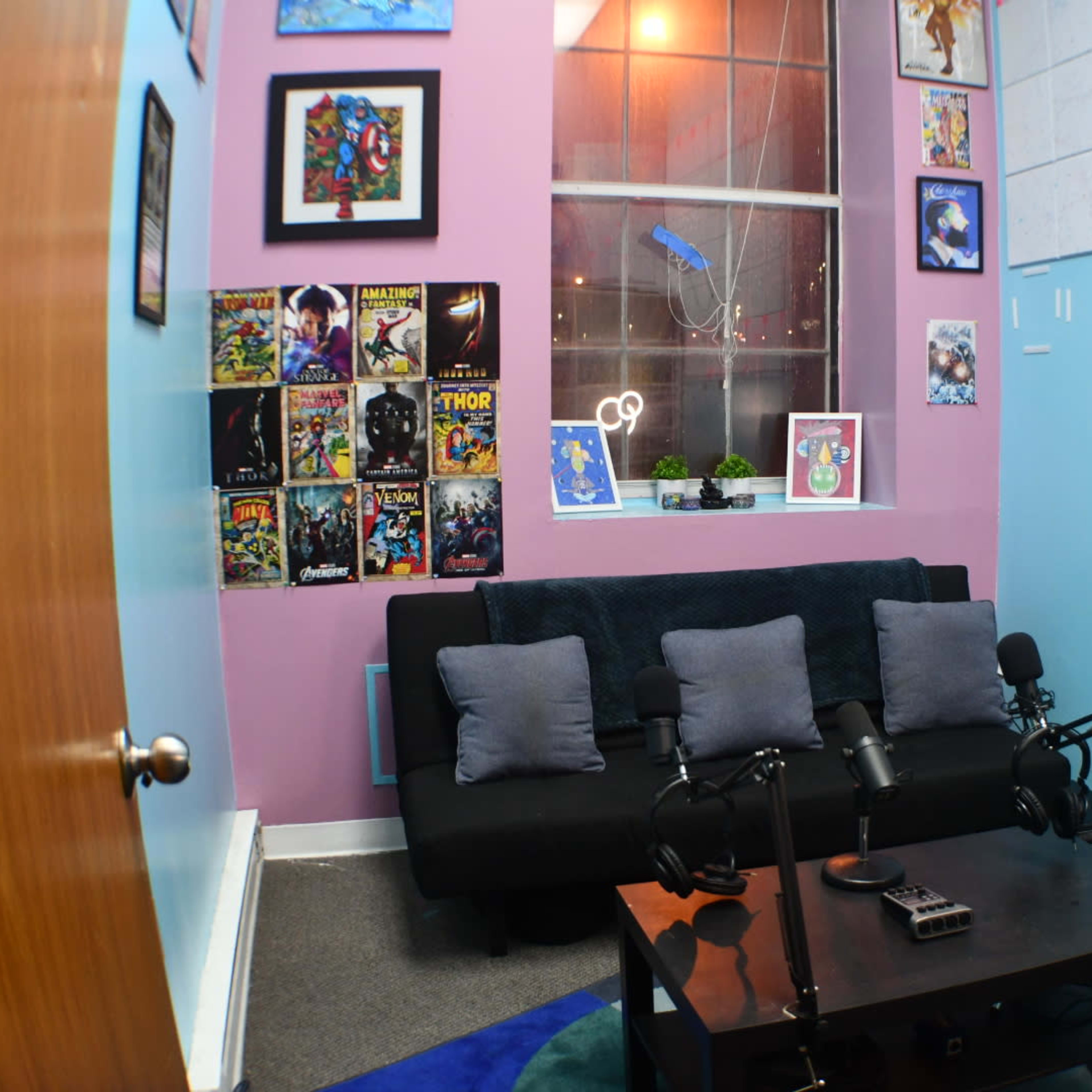 A small room with a sofa, two microphones on a table, and walls adorned with comic book art and posters.