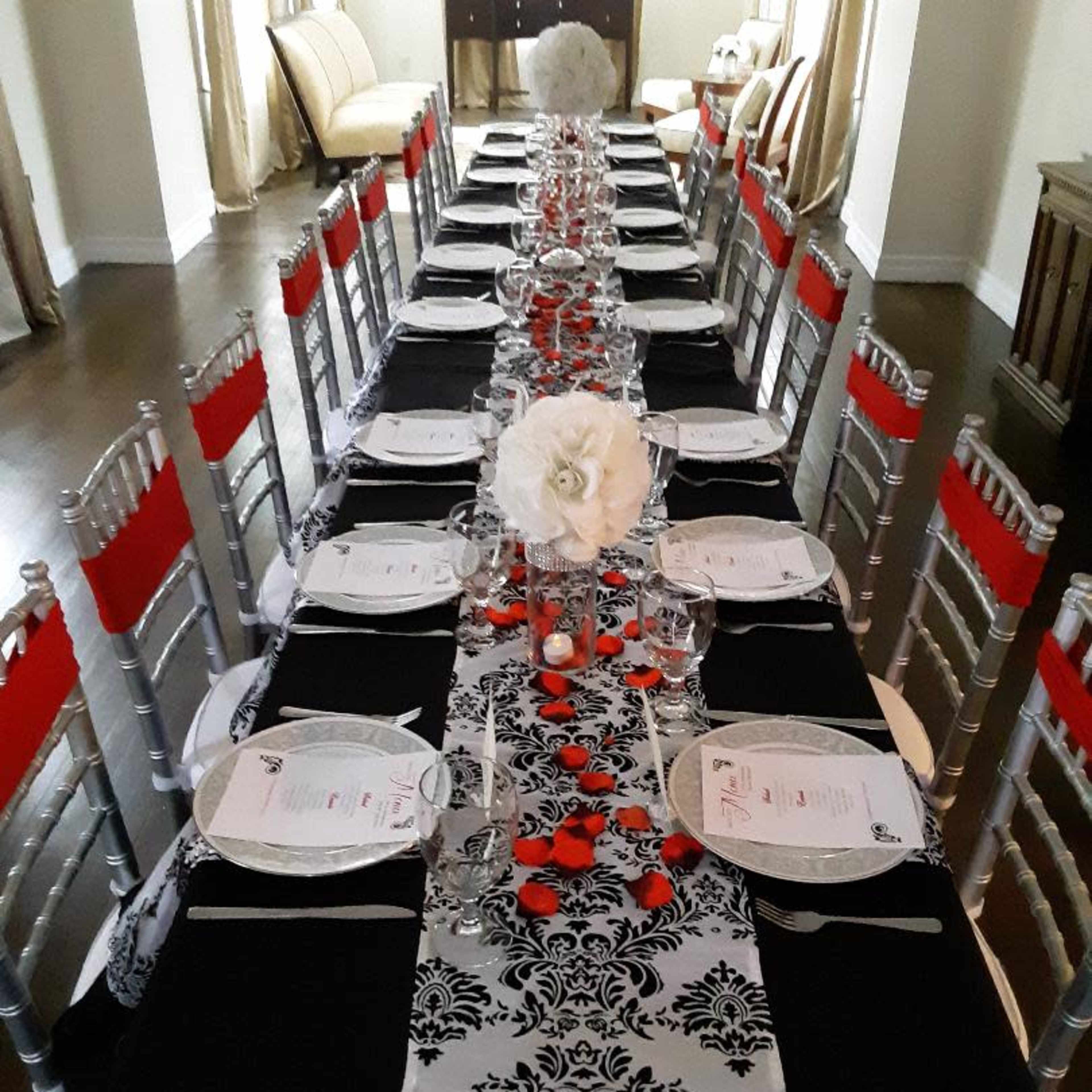 A long dining table is set with black and white tablecloths, red accents, plates, glasses, and floral centerpieces.