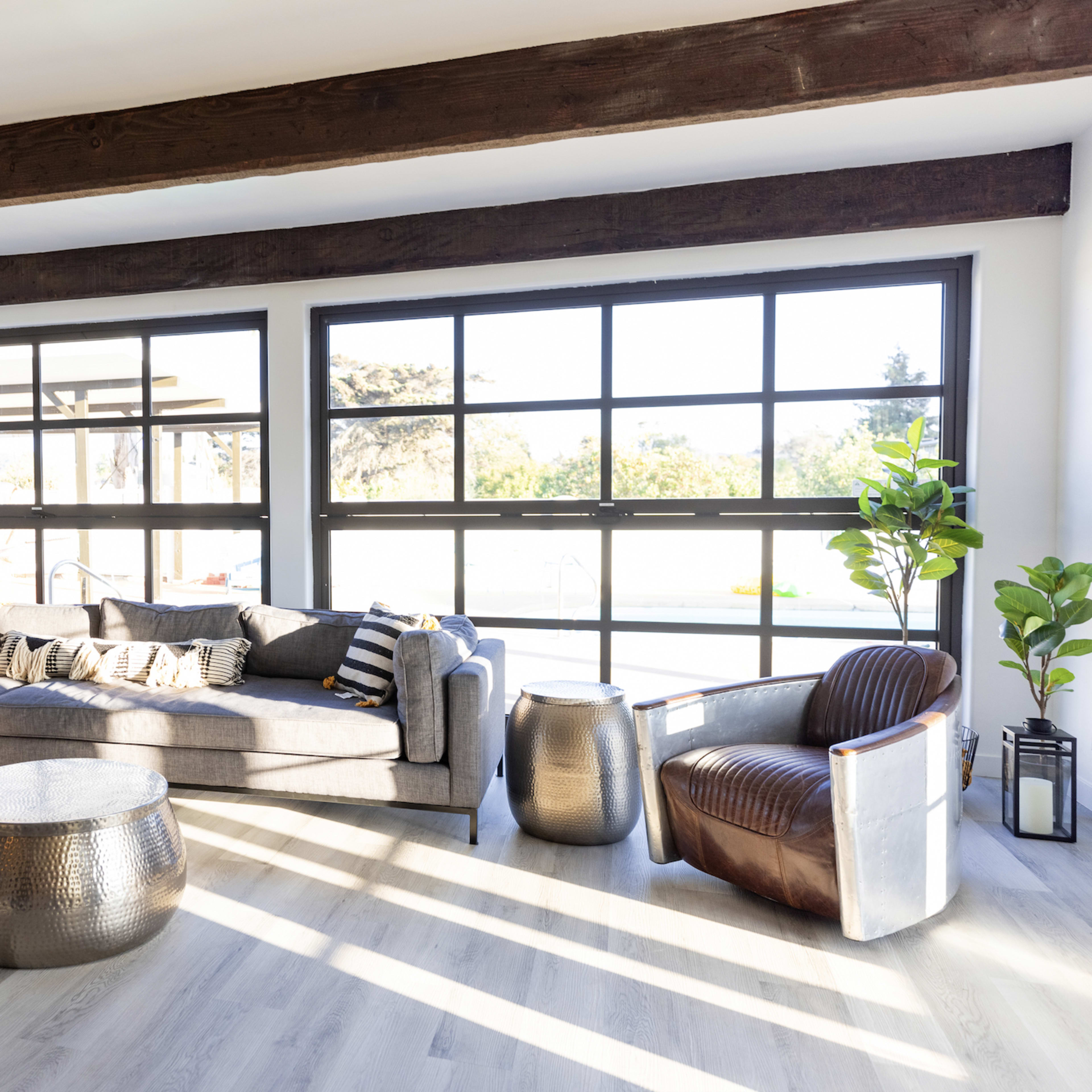 A modern living room features a sectional sofa, a round metallic coffee table, and large windows that allow natural light to illuminate the space.