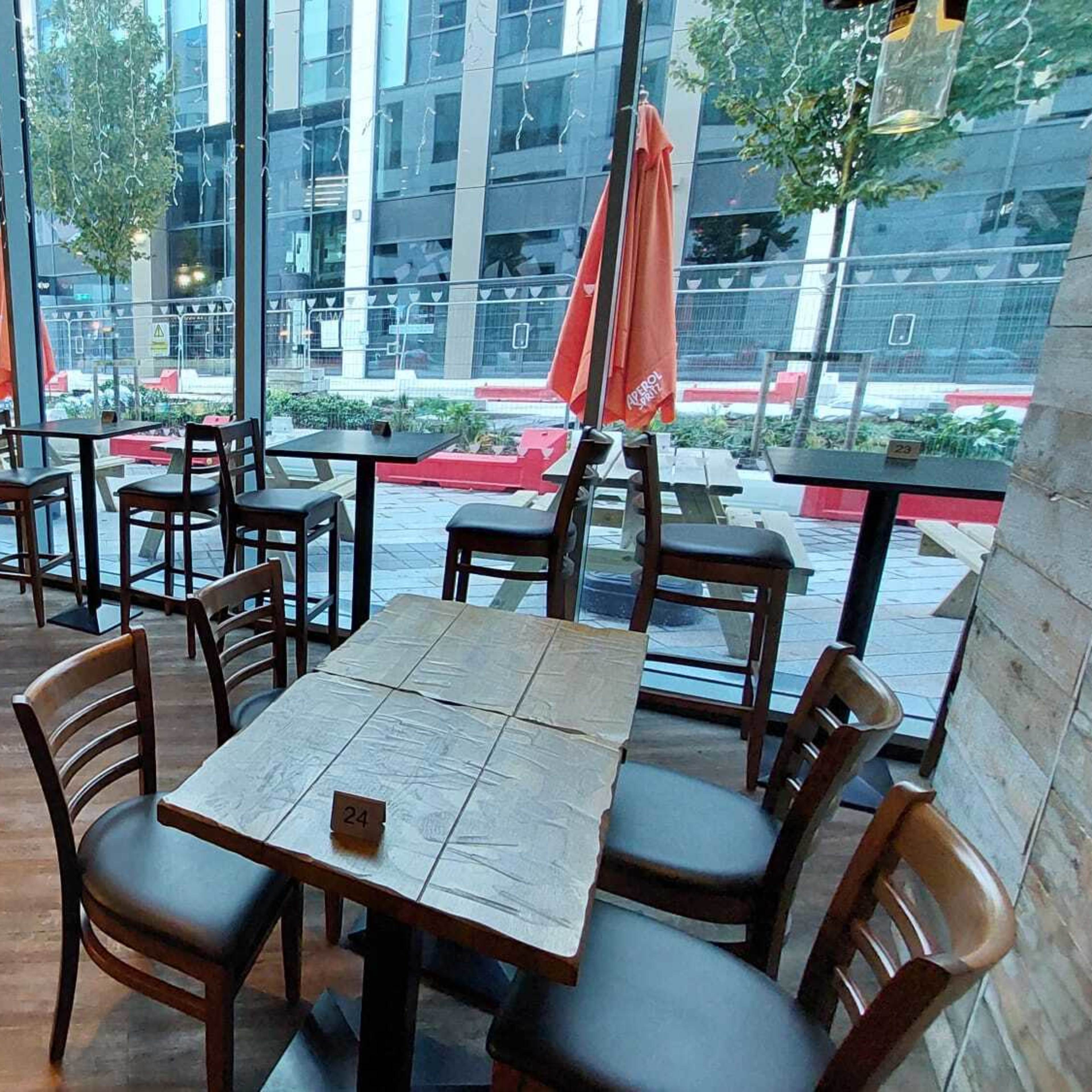 A modern restaurant interior with wooden tables and chairs arranged near large windows overlooking a city street.