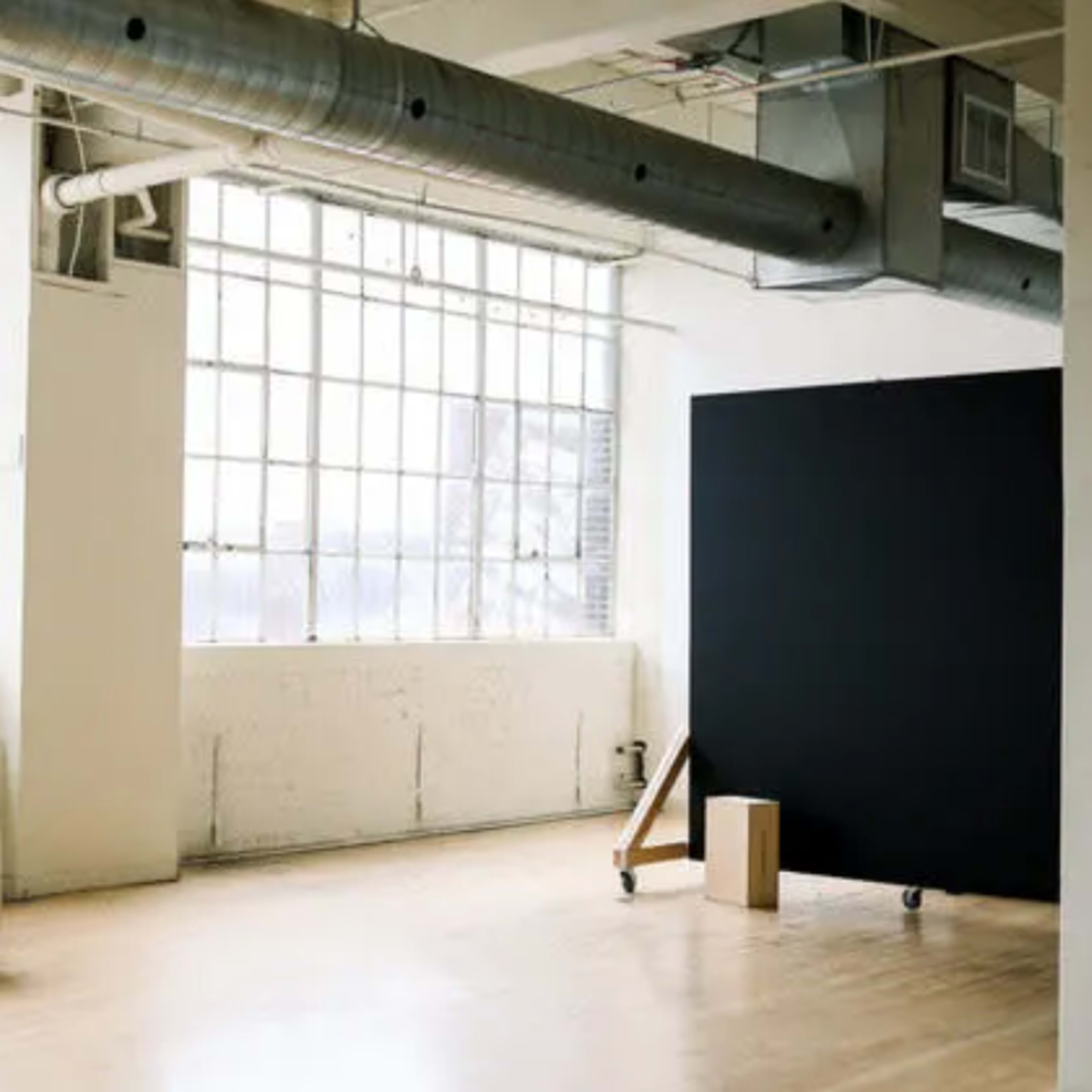 A bright, spacious room with large windows, featuring a white couch and a black backdrop on wheels.