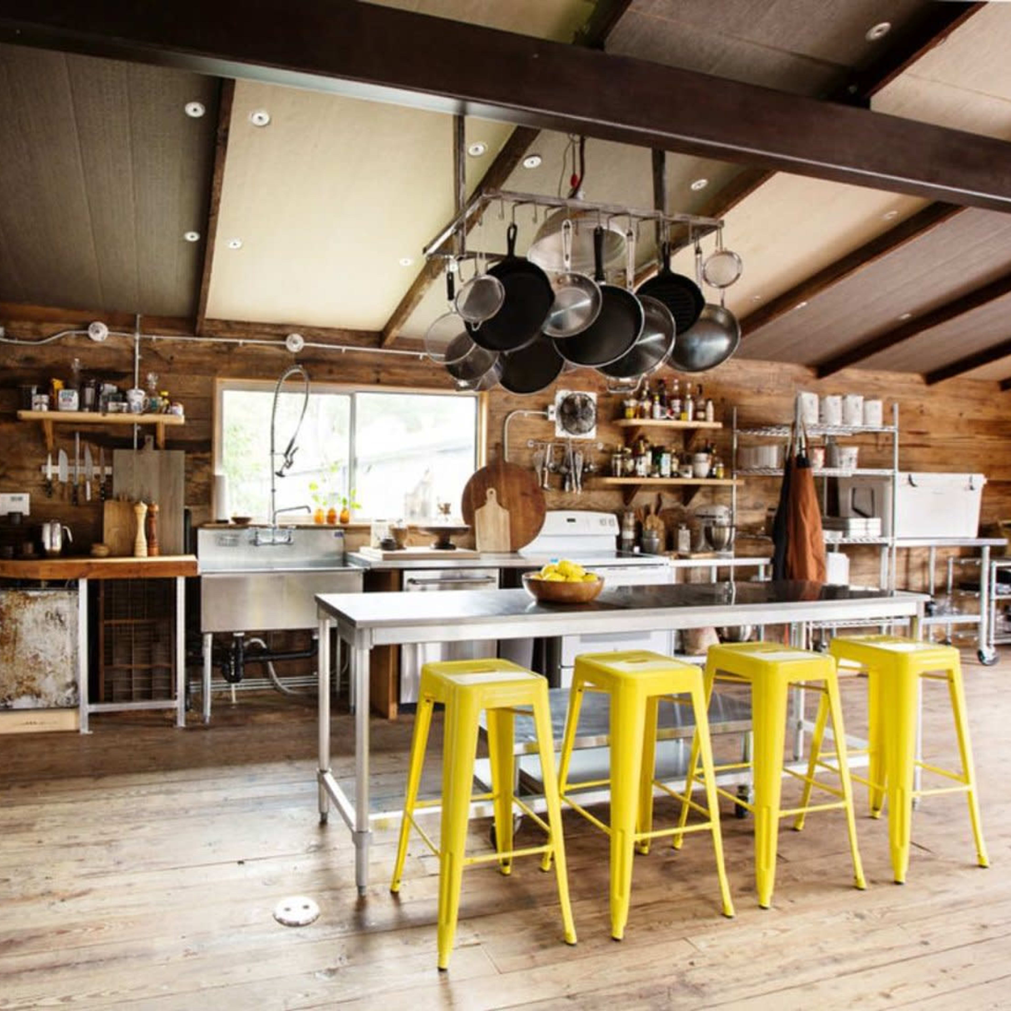 A modern kitchen featuring stainless steel appliances, wooden accents, and bright yellow bar stools arranged around an island.