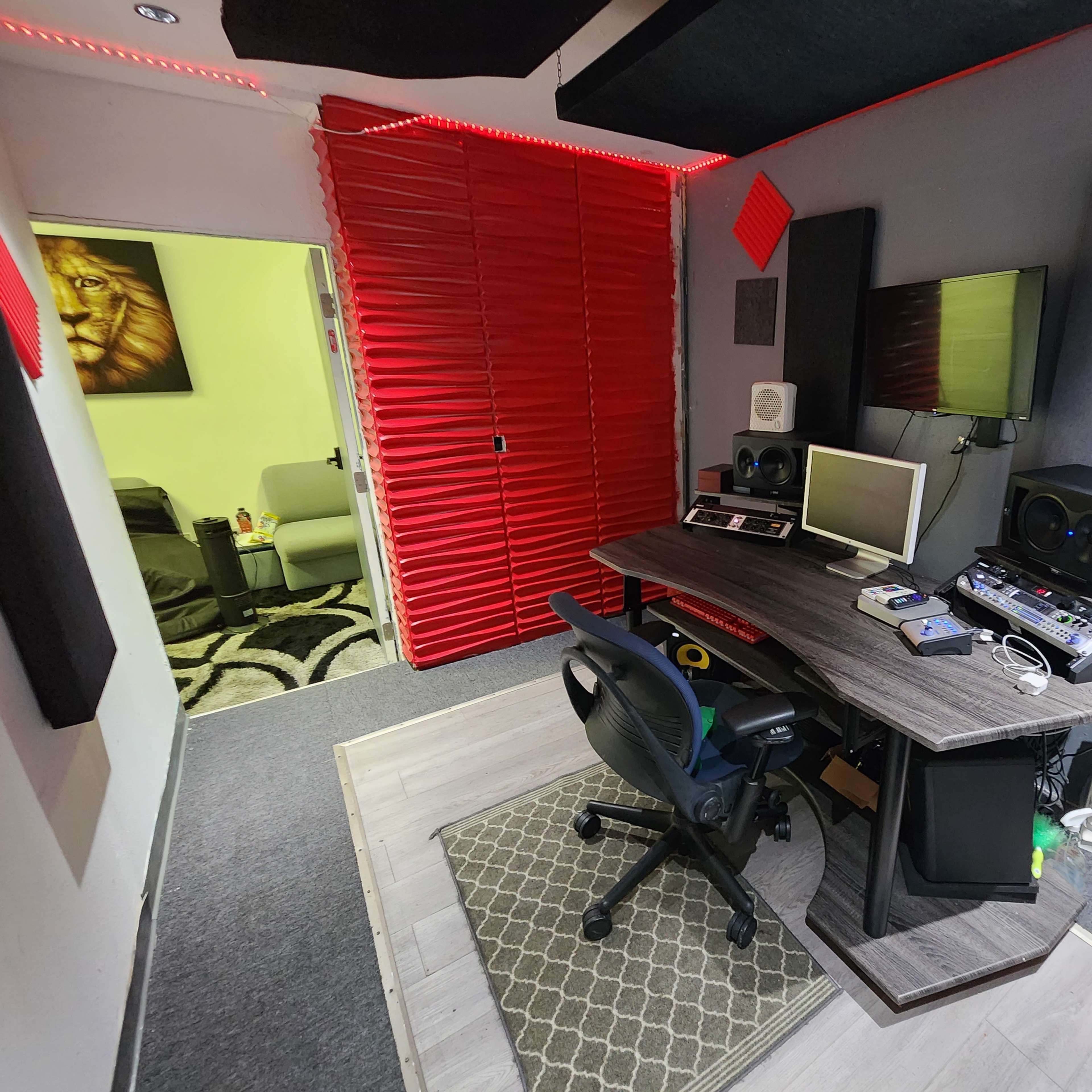 A compact recording studio features a desk with audio equipment, surrounded by soundproofing panels and red accent walls.