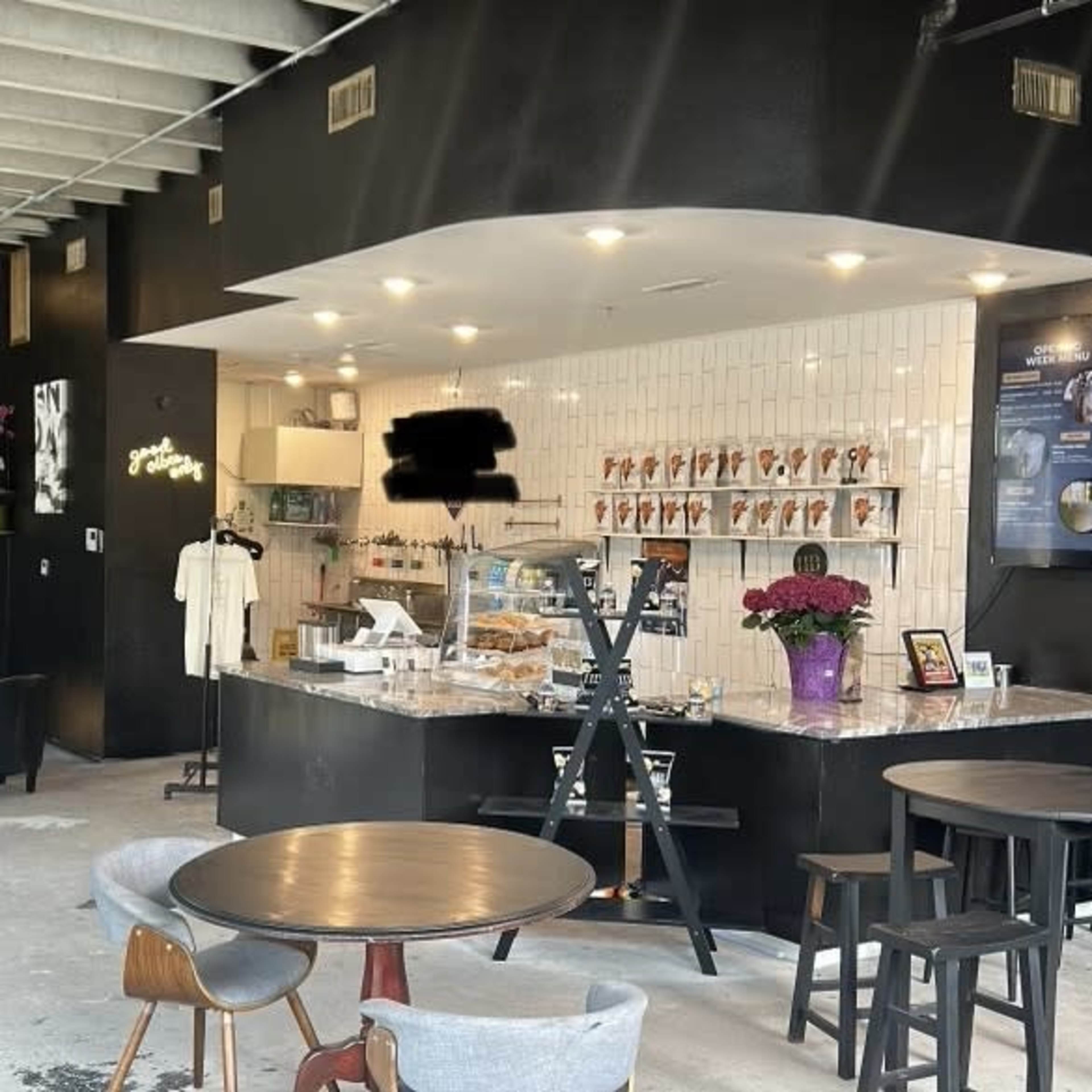 A modern café interior with a black and white color scheme, featuring a service counter, tables, and various seating arrangements.