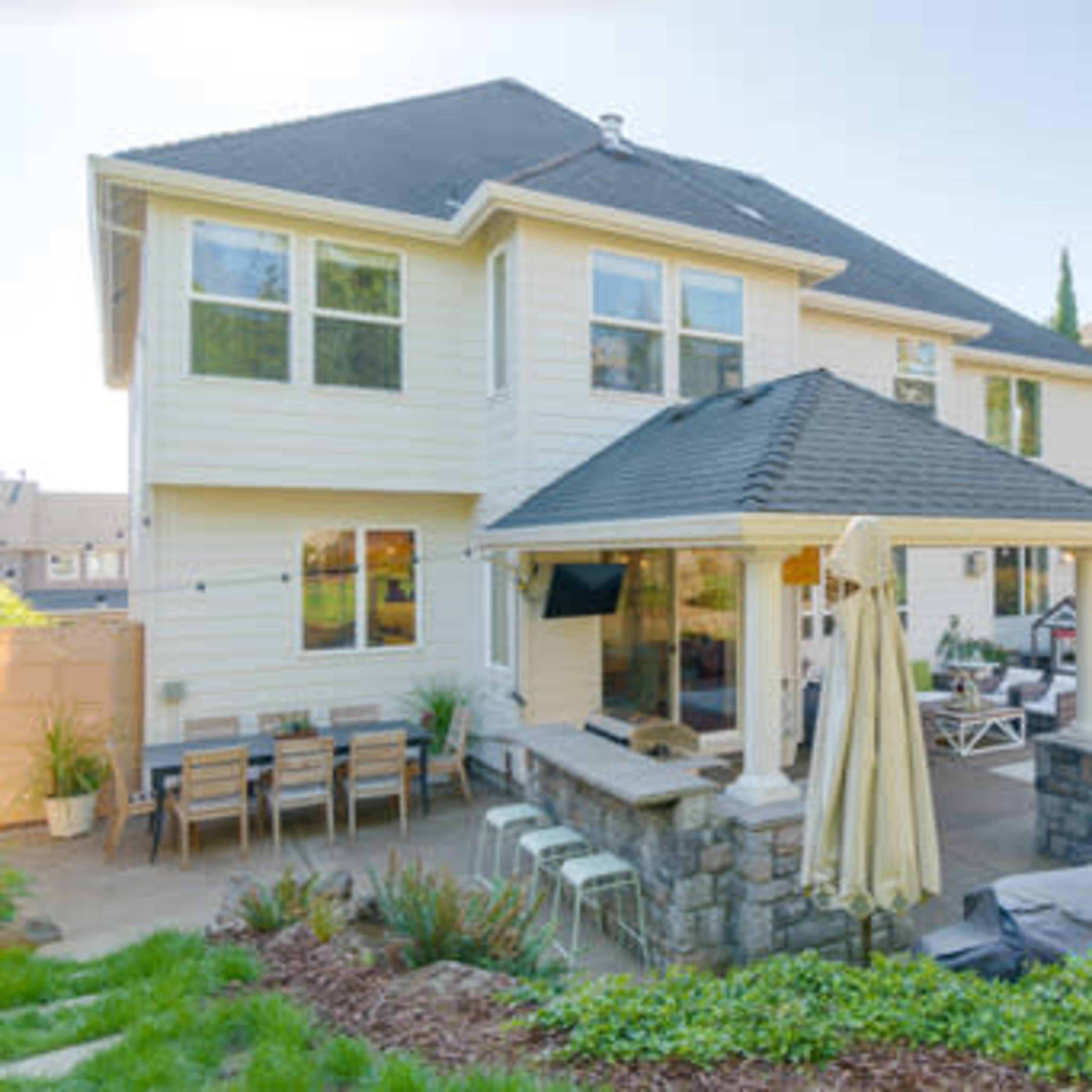A two-story house with a patio area featuring a stone wall and outdoor seating in a landscaped backyard.