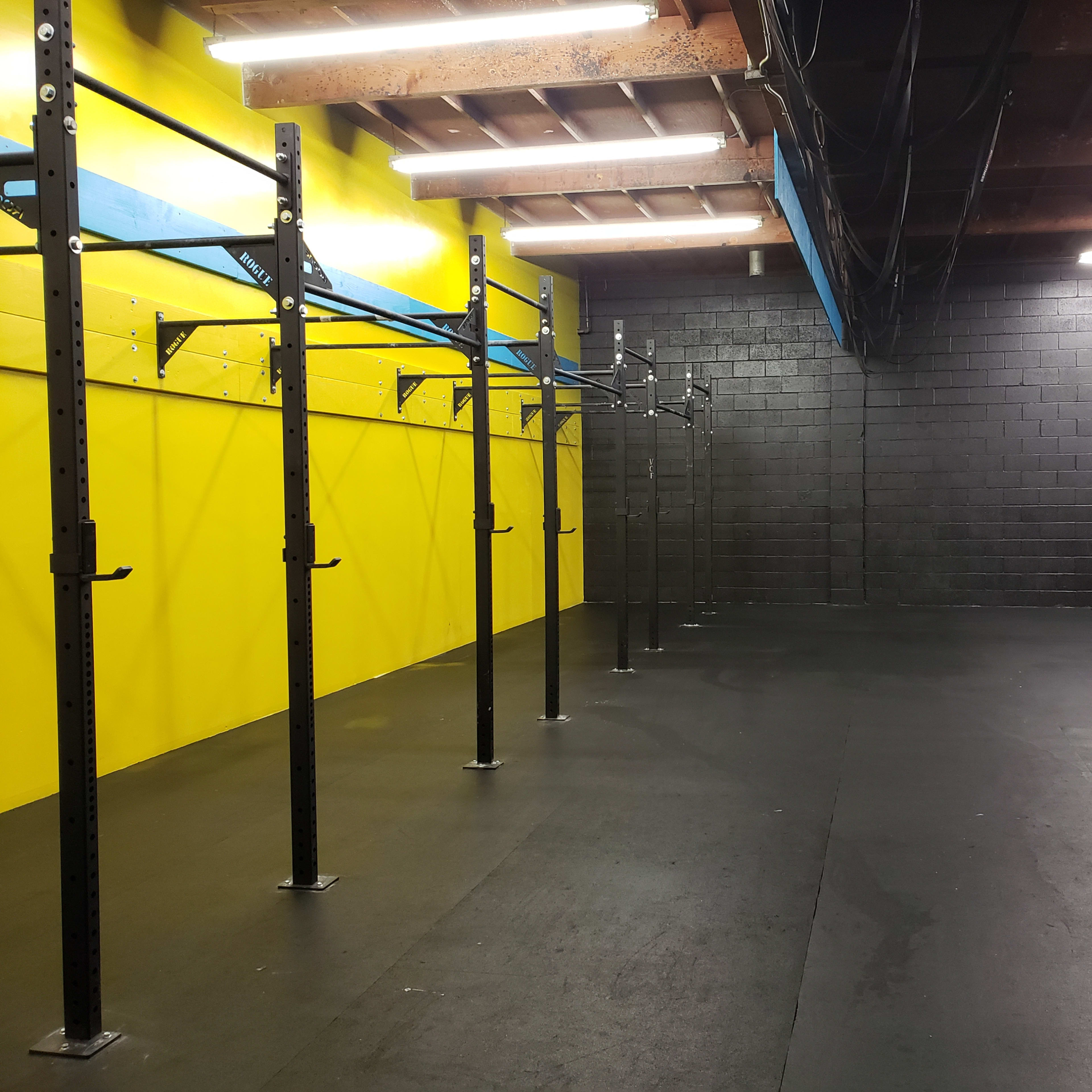 A gym interior with black walls and a bright yellow accent wall, featuring pull-up bars and ropes for exercise.