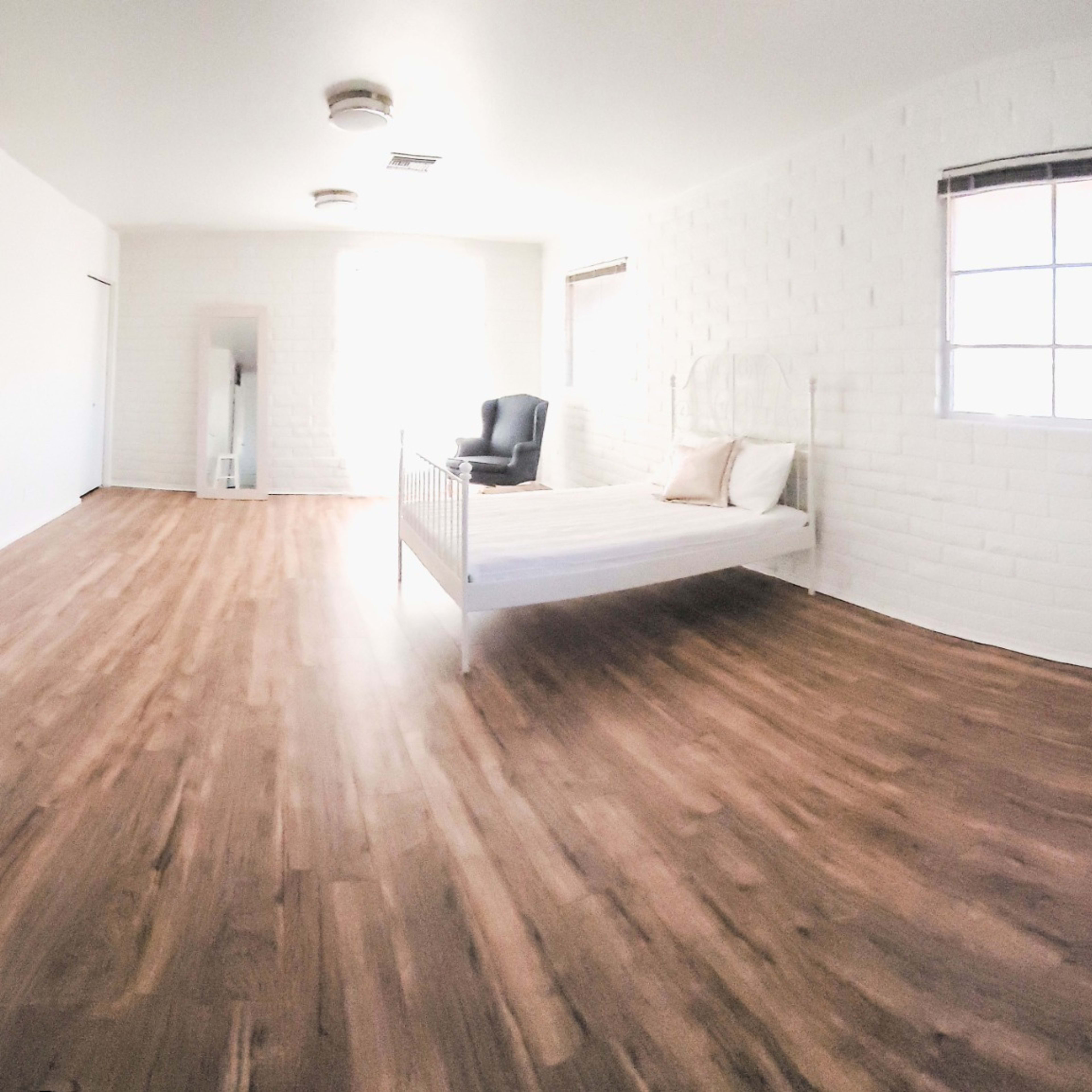 A spacious, minimalist living area with white walls, wooden flooring, and a mix of furniture including a bed, a green sofa, and a small table with chairs.