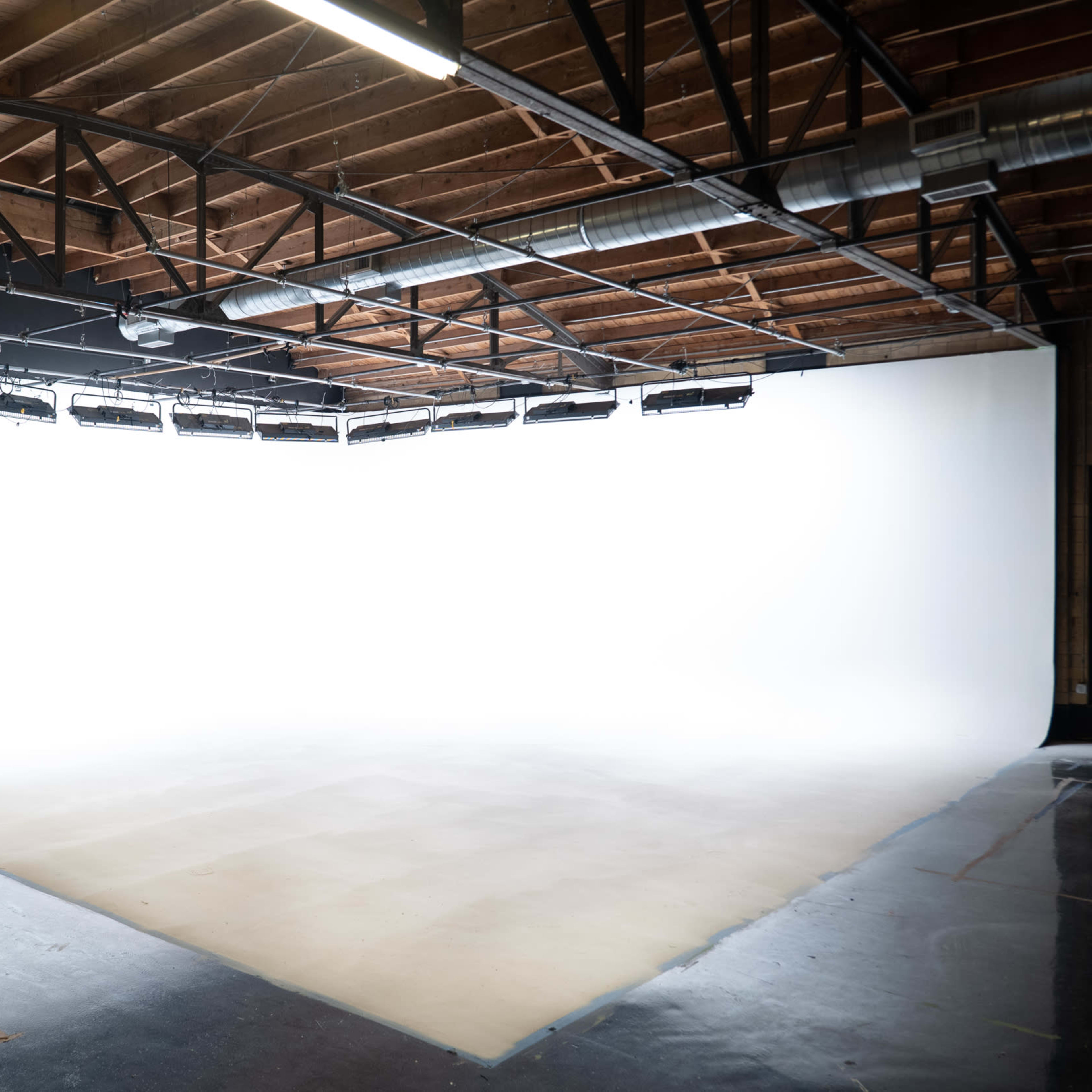 A spacious photography studio with a seamless white backdrop and a polished floor.