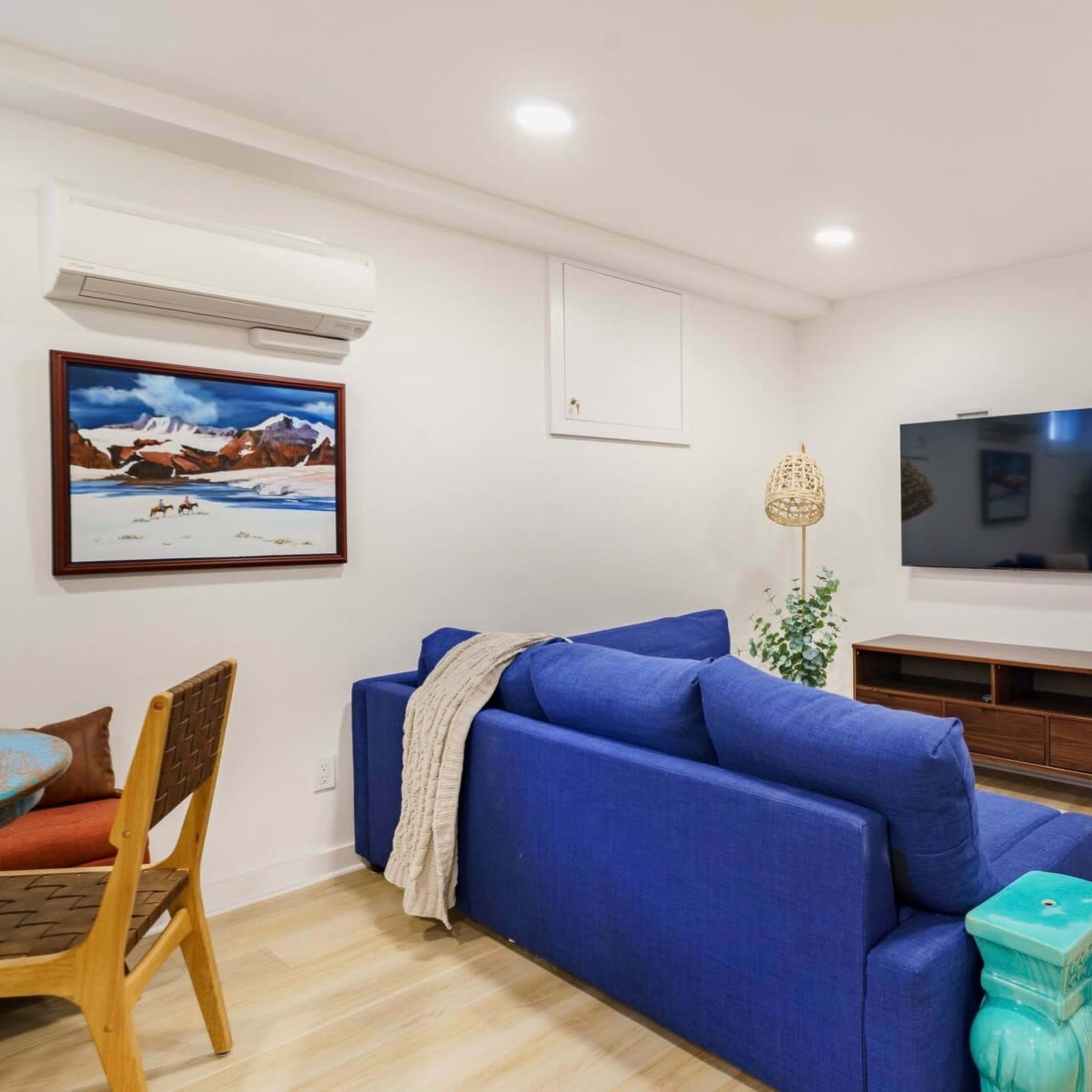 A small living room with a blue sofa, a mounted television on a wooden stand, and a doorway leading to a bedroom.