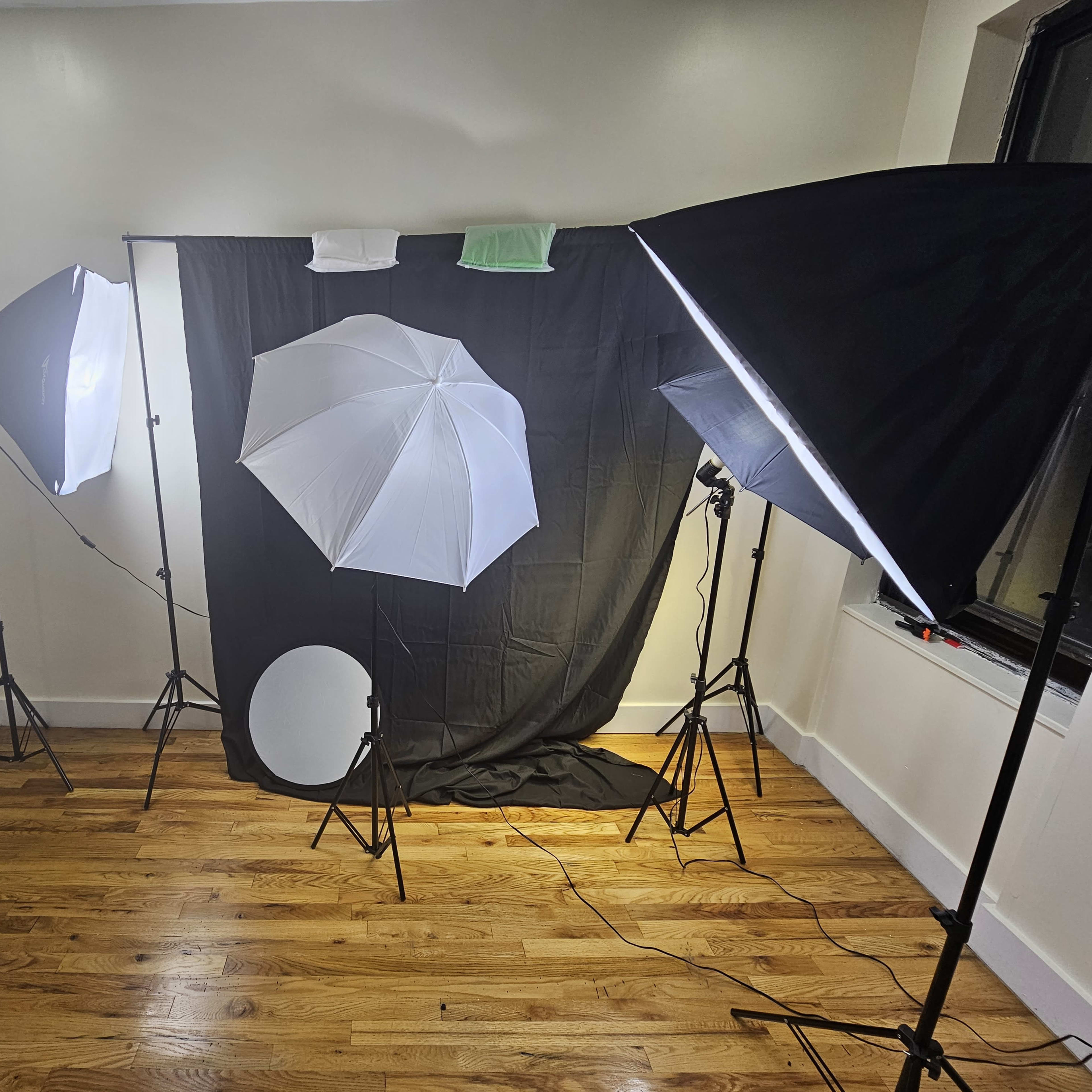 A well-lit photography setup featuring two softbox lights, a round reflector, and a black background.