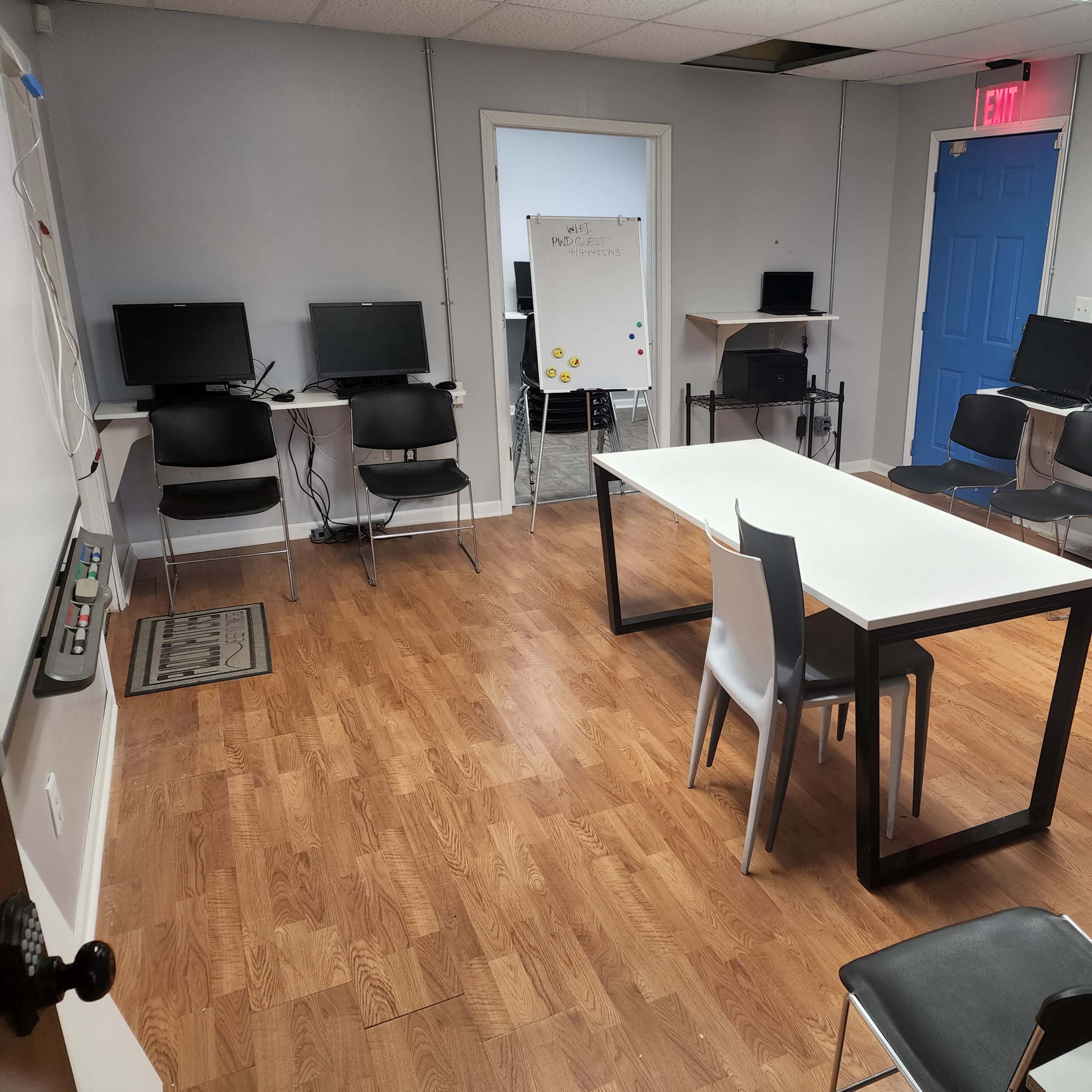 A classroom with a rectangular table surrounded by chairs, equipped with several computers along the walls.