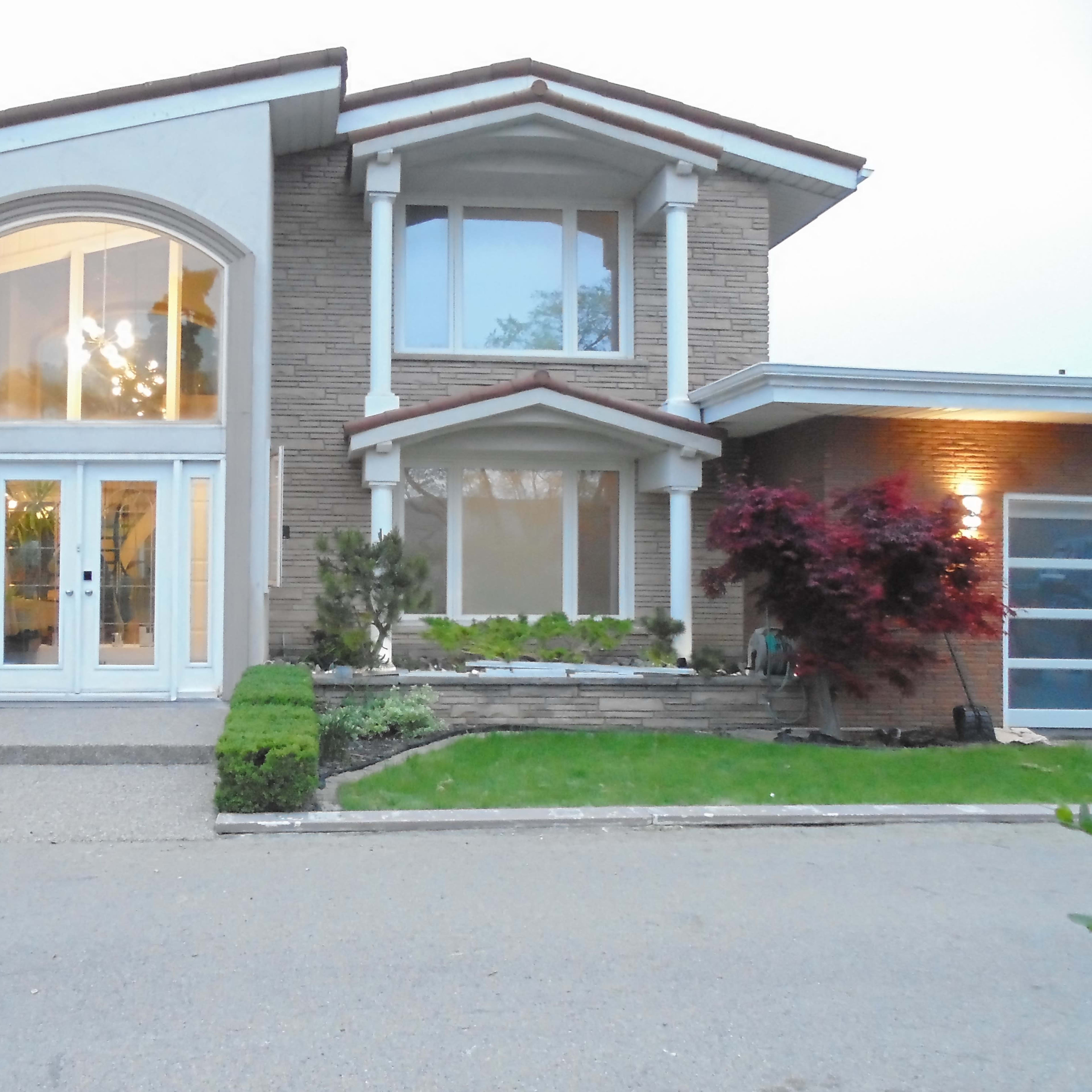 A modern two-story house with a large front entrance, a neatly landscaped yard, and large windows.