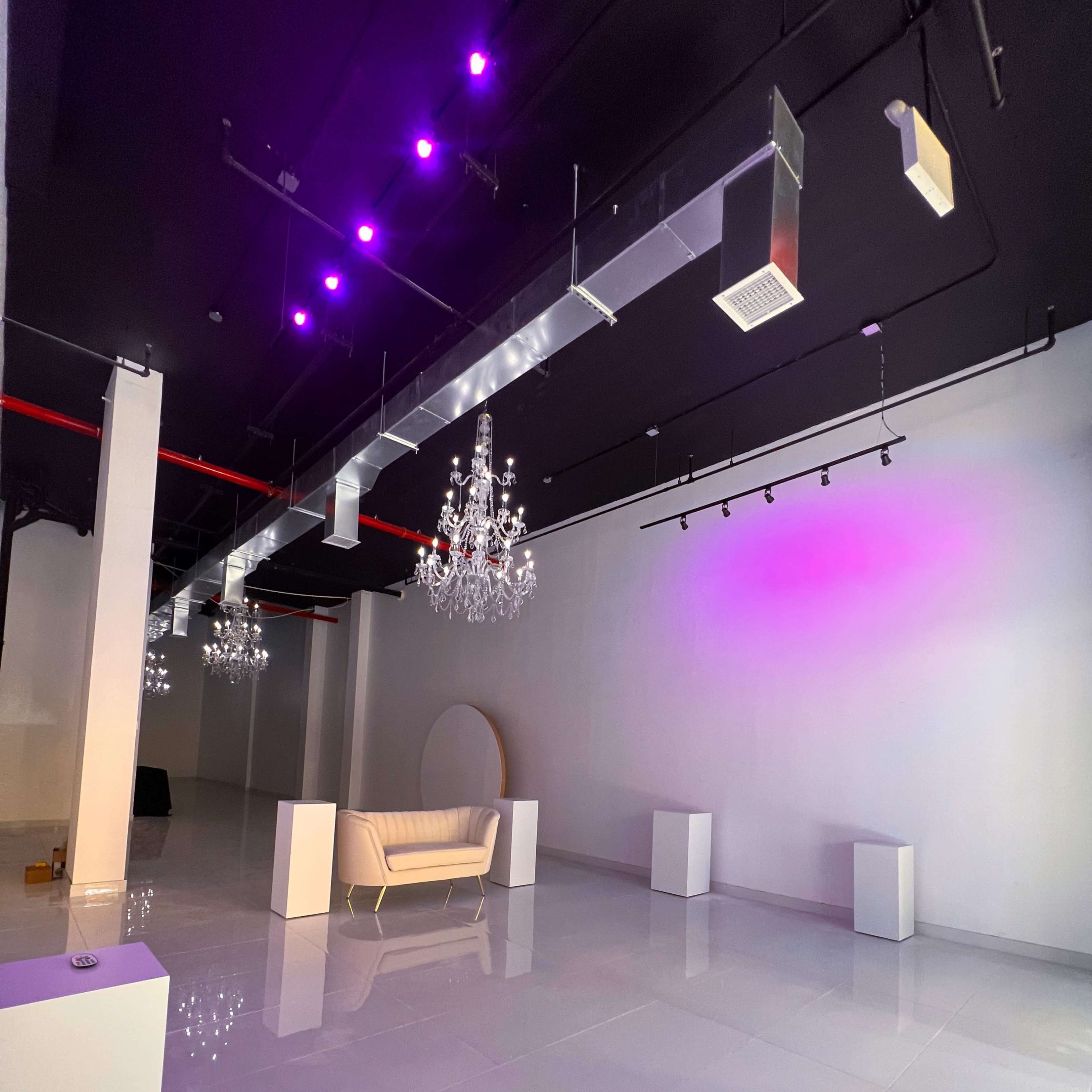 An empty, modern event space with white walls, a glossy floor, and chandeliers hanging from the ceiling.