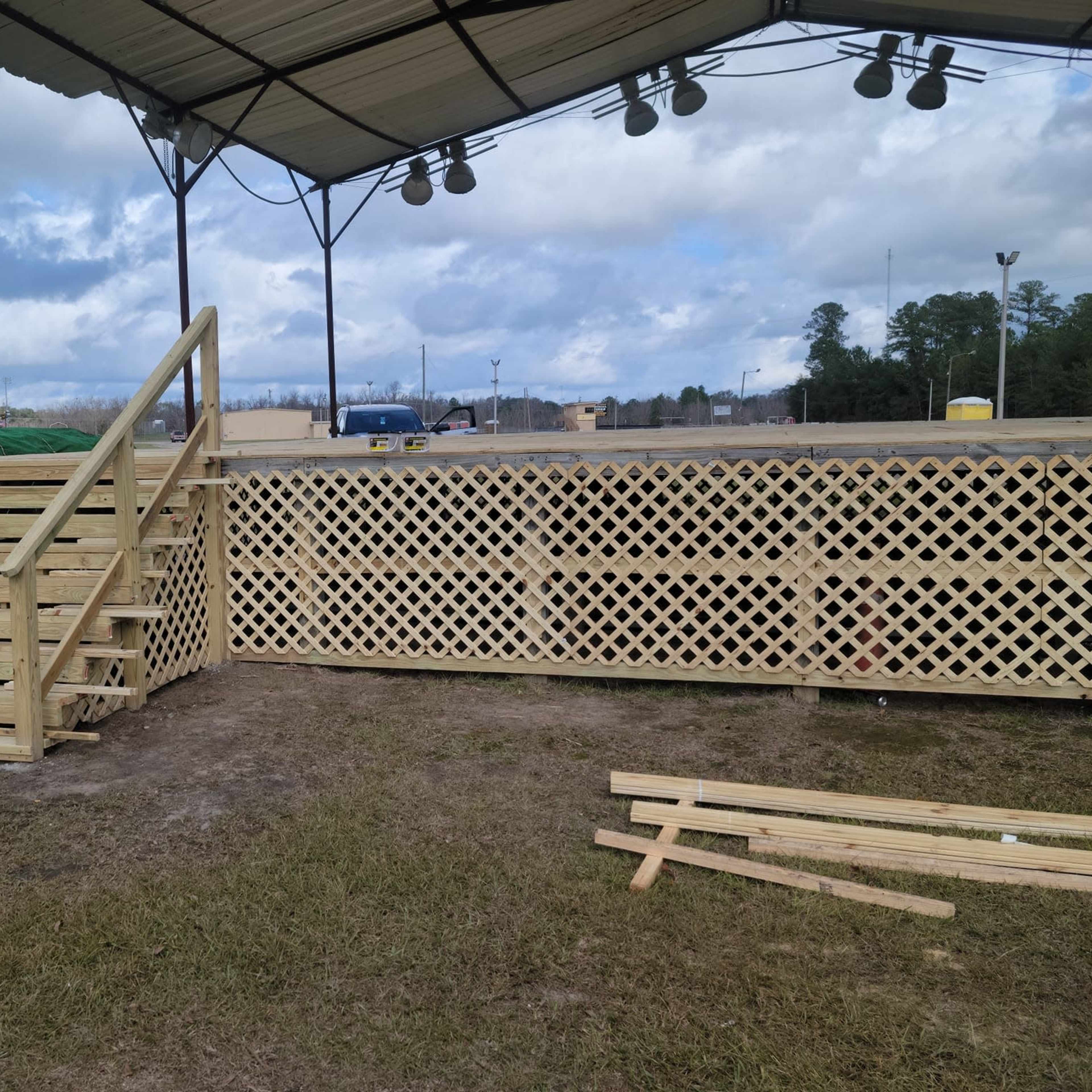 A wooden deck with a set of stairs and a lattice enclosure under a covered area, with cloudy skies in the background.