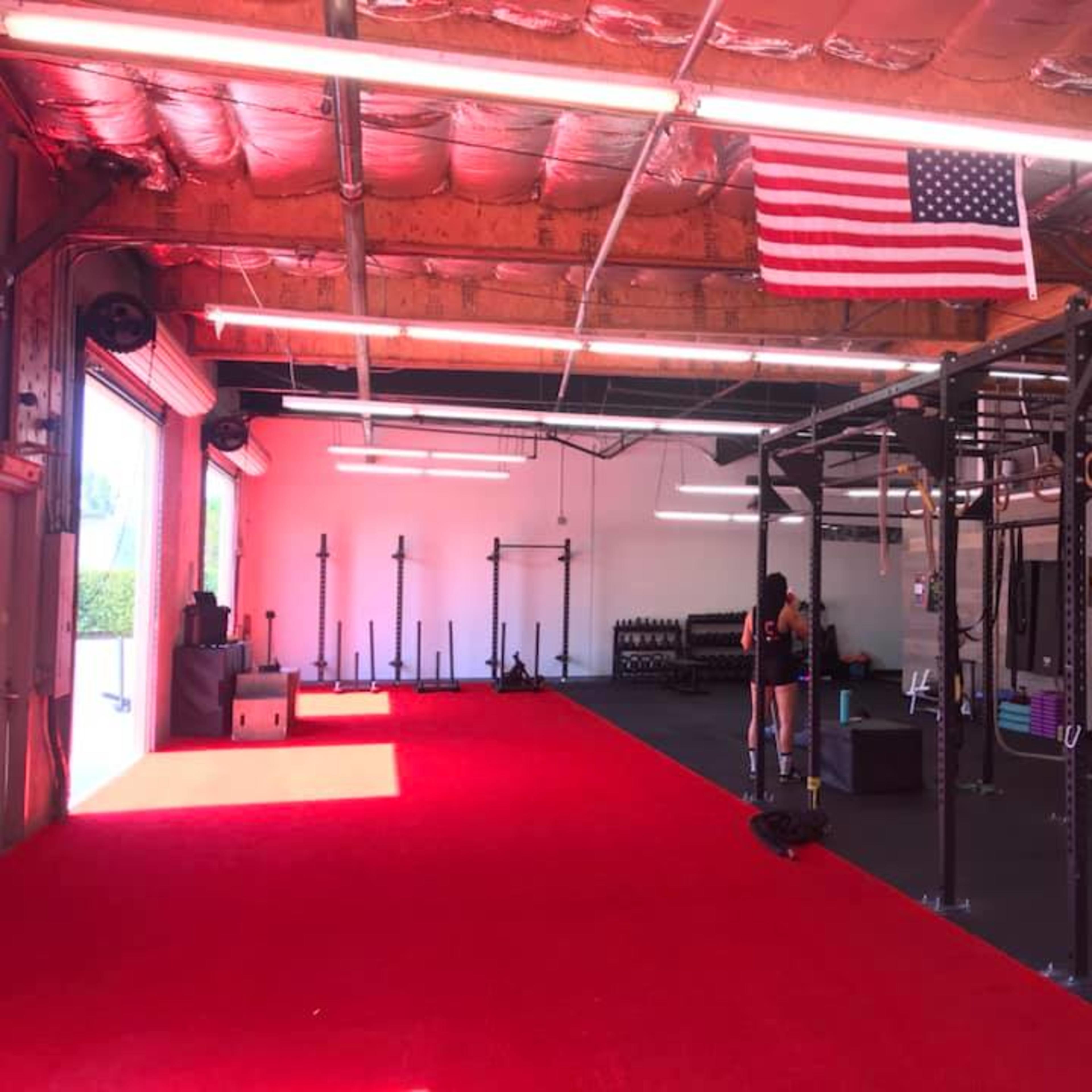 An interior of a gym with red carpet, exercise equipment, and an American flag hung from the ceiling.