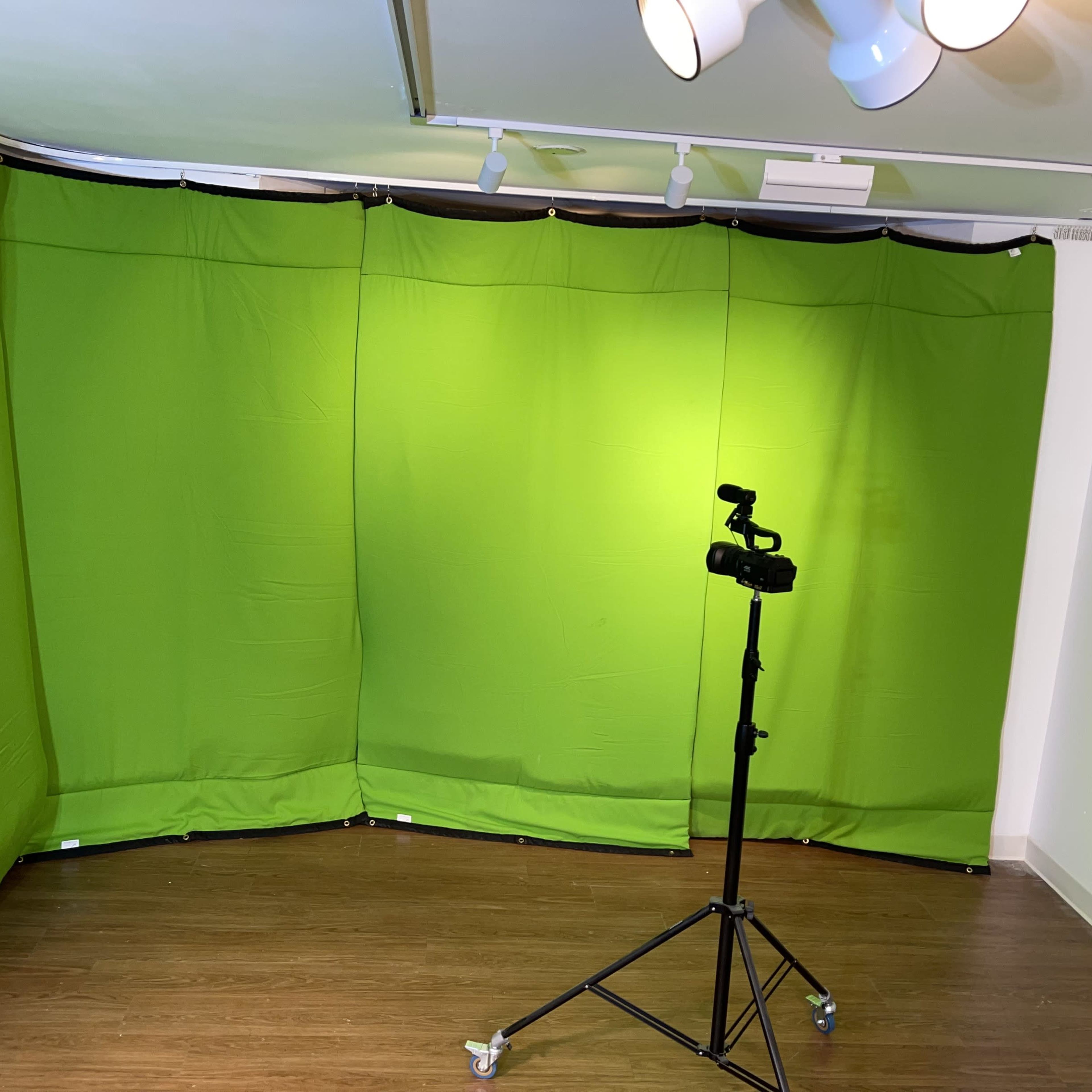 A green screen setup in a room with wooden flooring and a camera on a tripod.