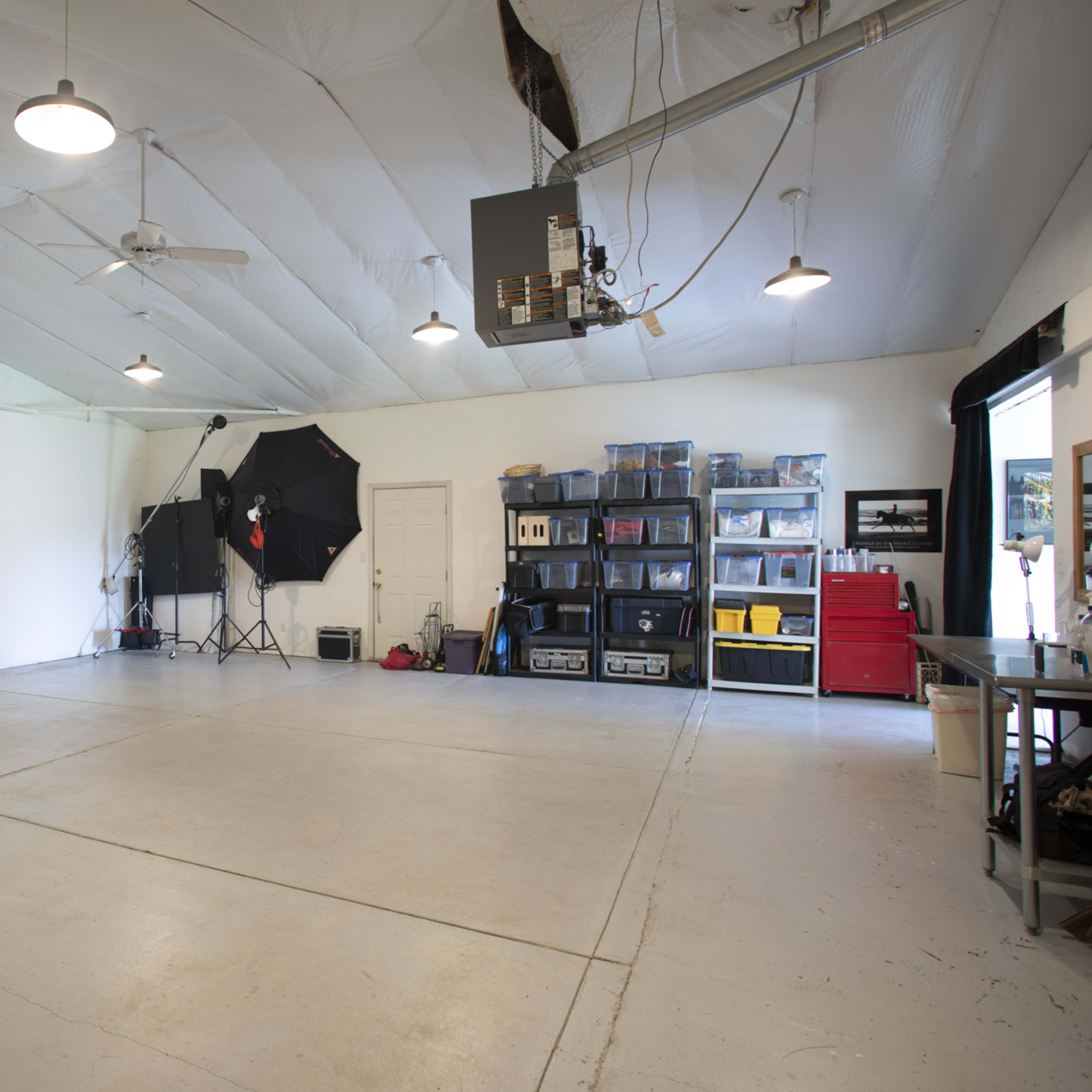 A spacious, well-lit garage with a concrete floor, photography equipment, and storage units along the walls.