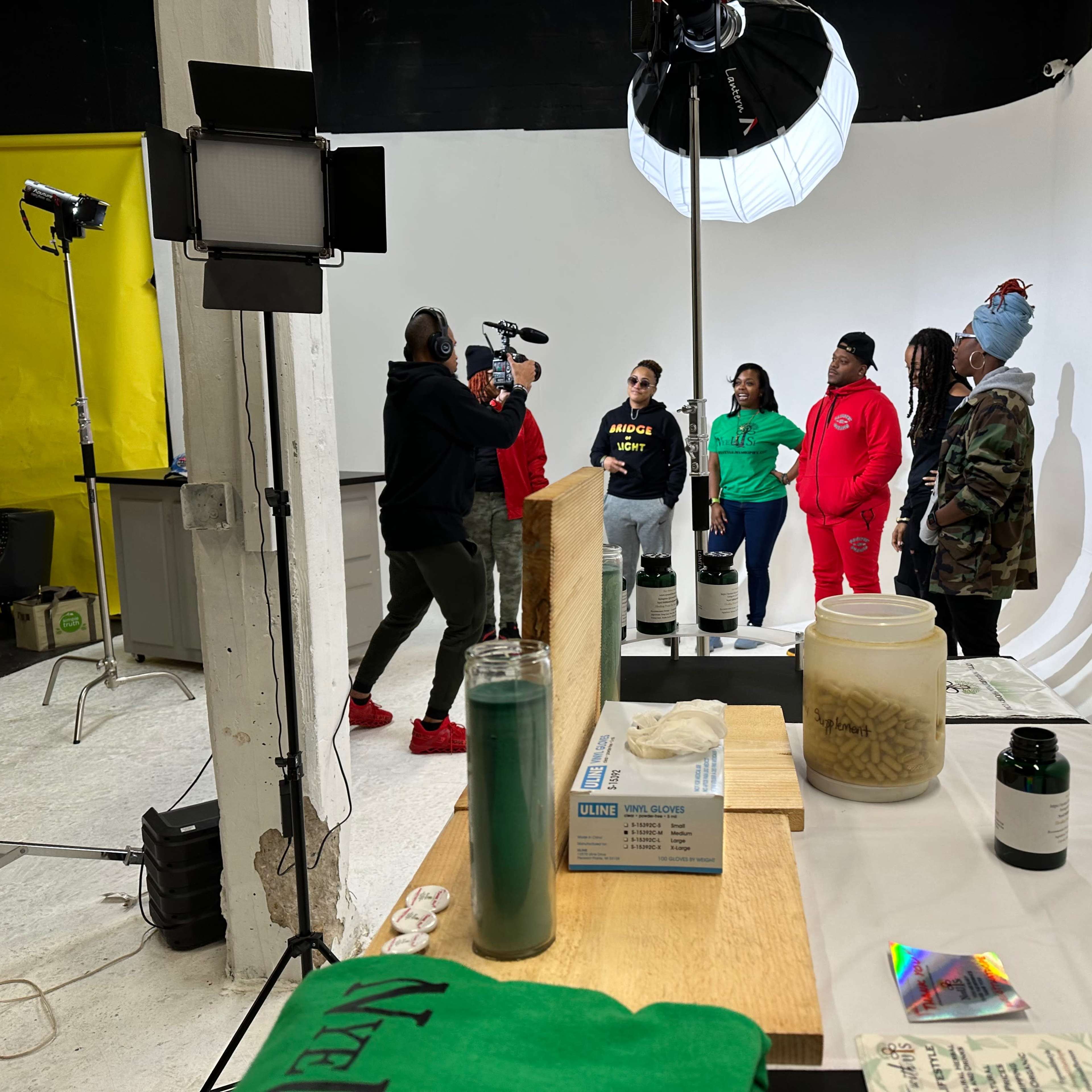 A group of people stands in front of a camera and microphone in a studio with a white backdrop.