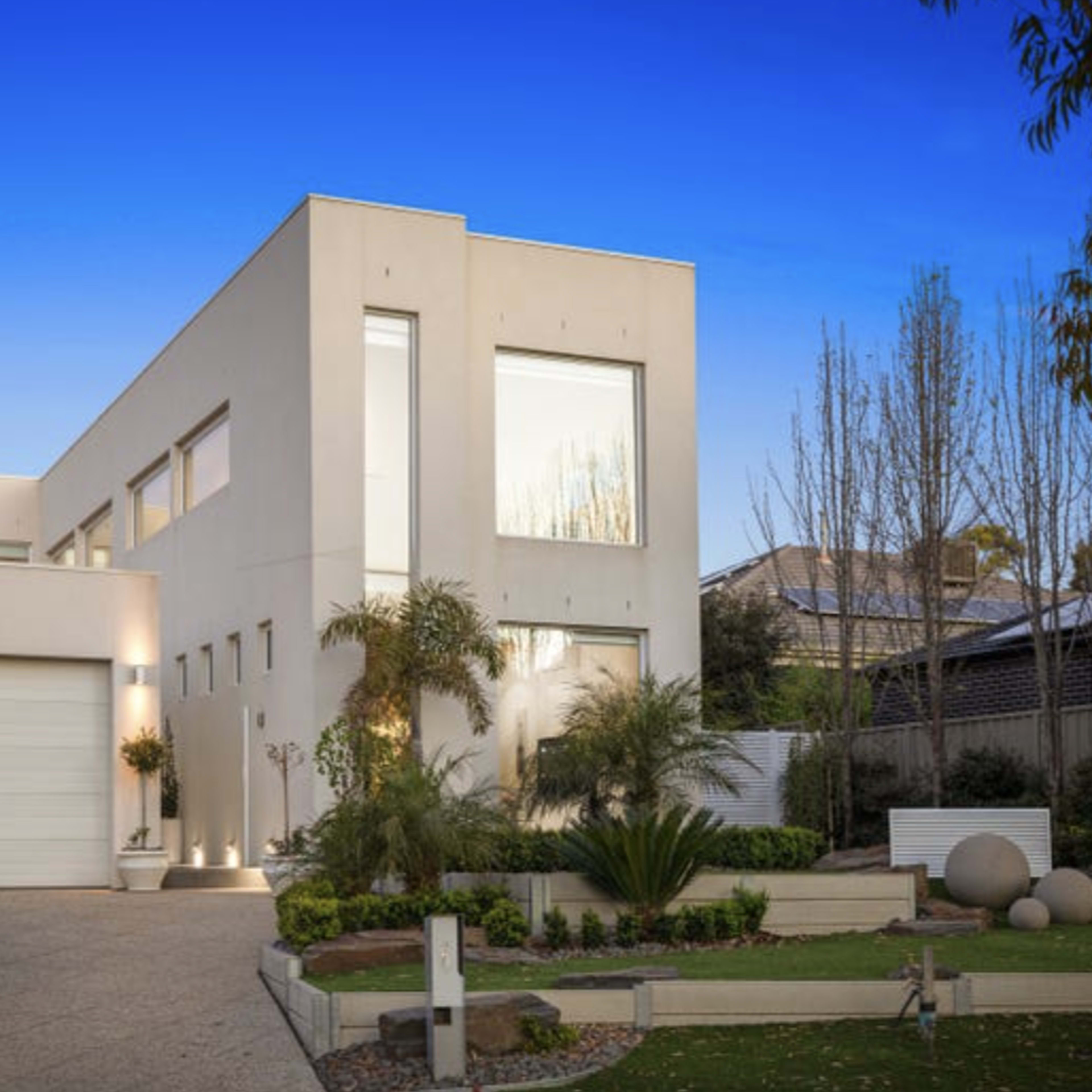 A modern two-story house with large windows and a landscaped front yard.