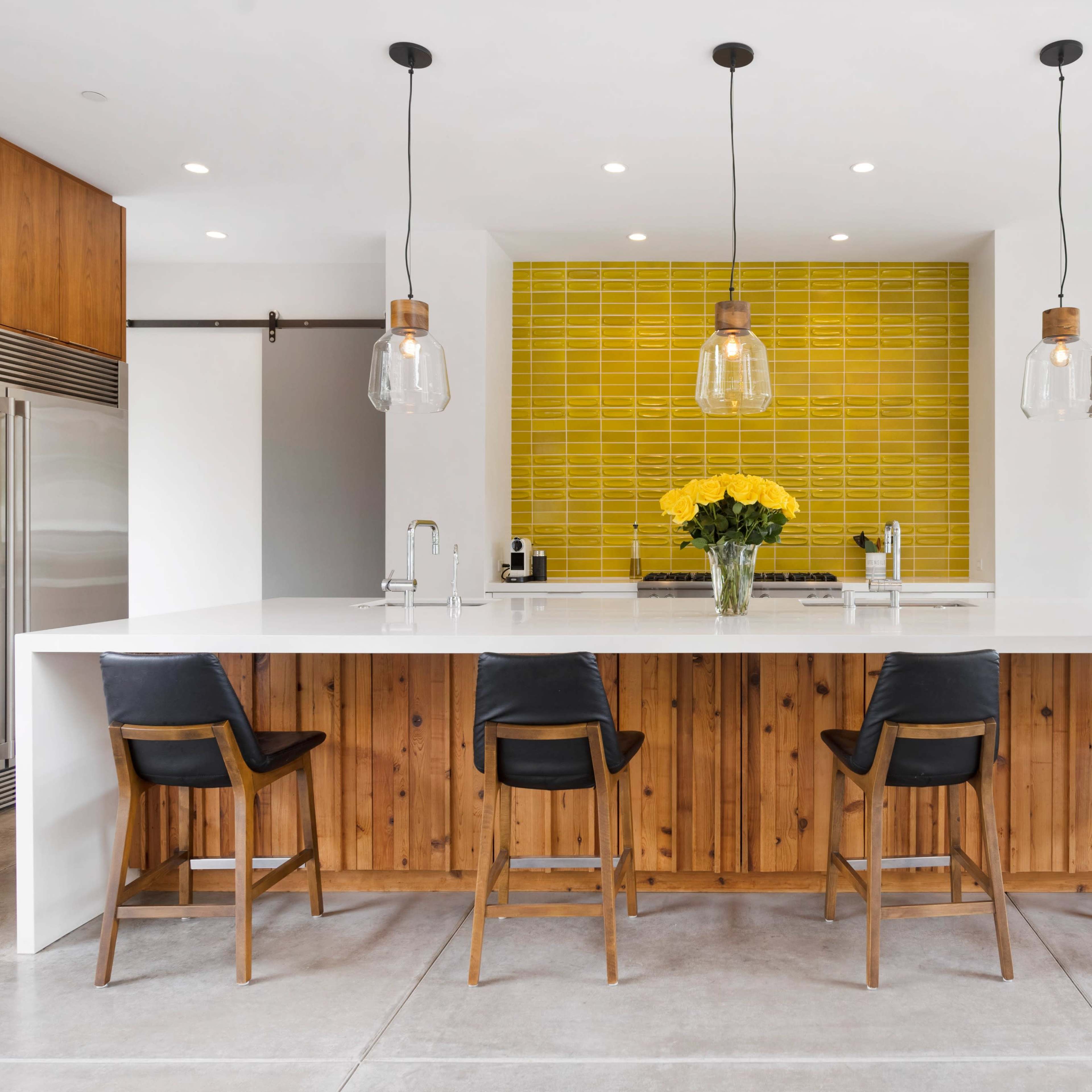 The kitchen features a modern island with bar stools, wooden cabinetry, and a bright yellow backsplash.