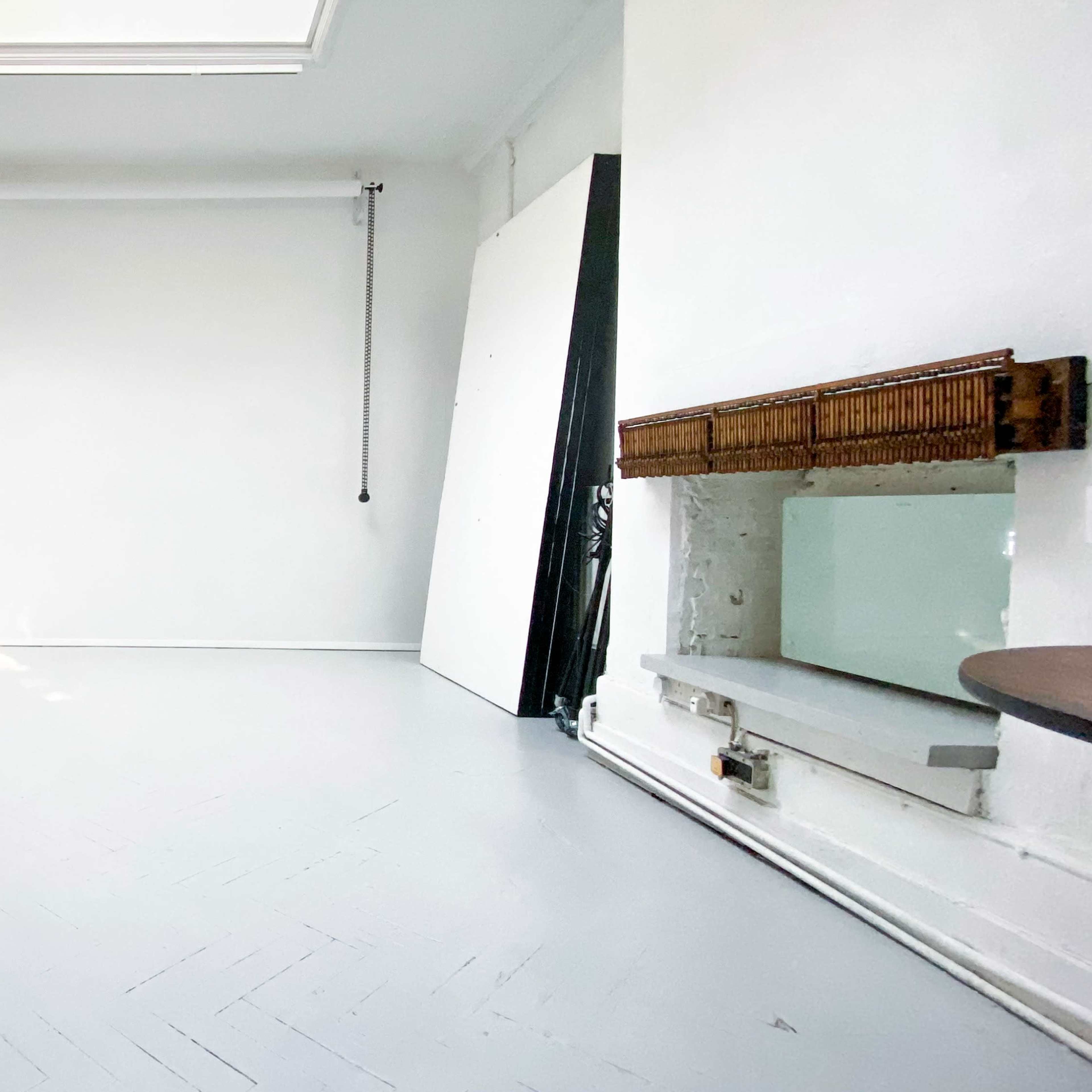 A bright, empty room with white walls, a skylight, and a large mirror on one side.