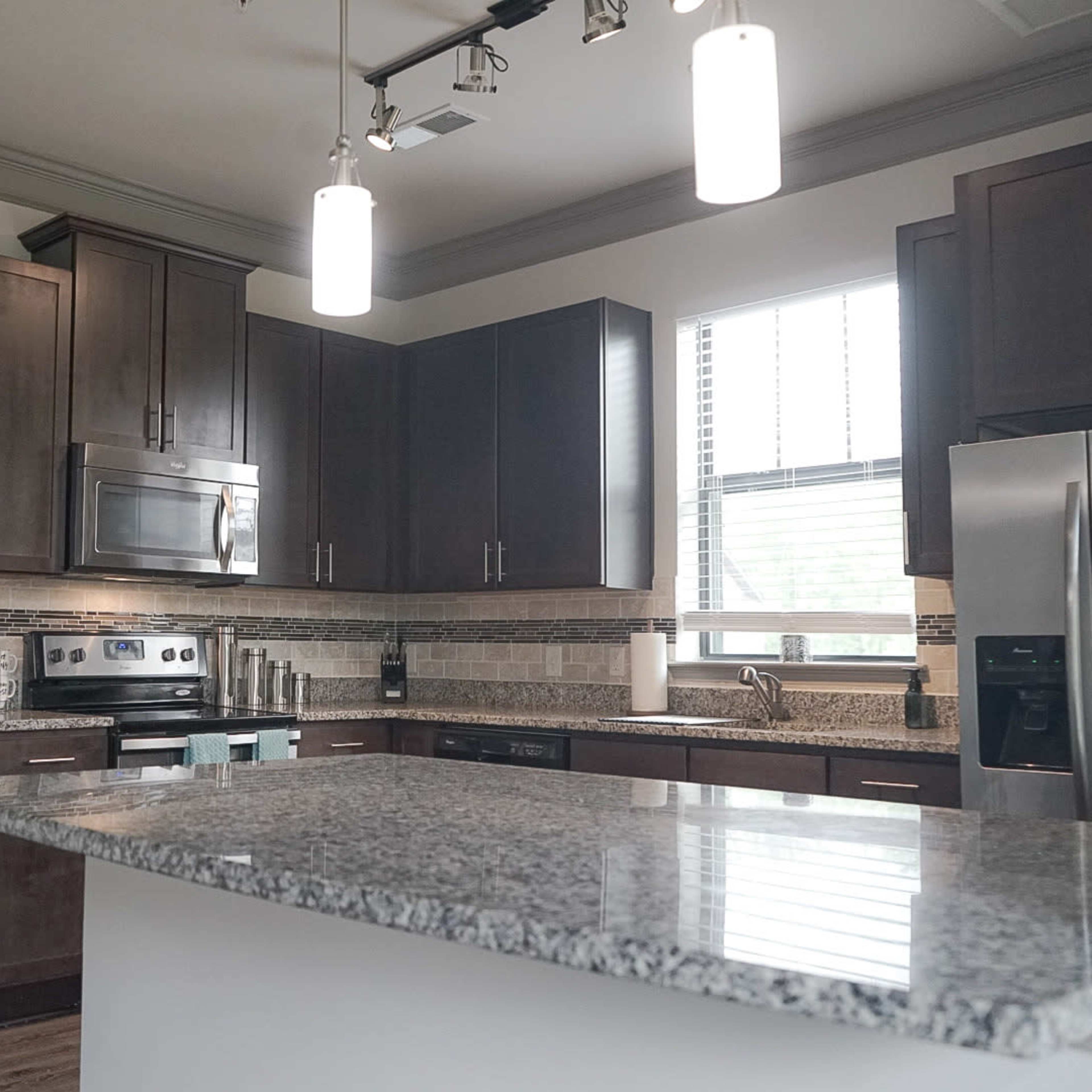 A modern kitchen featuring dark wooden cabinets, stainless steel appliances, and a granite countertop with bar seating.