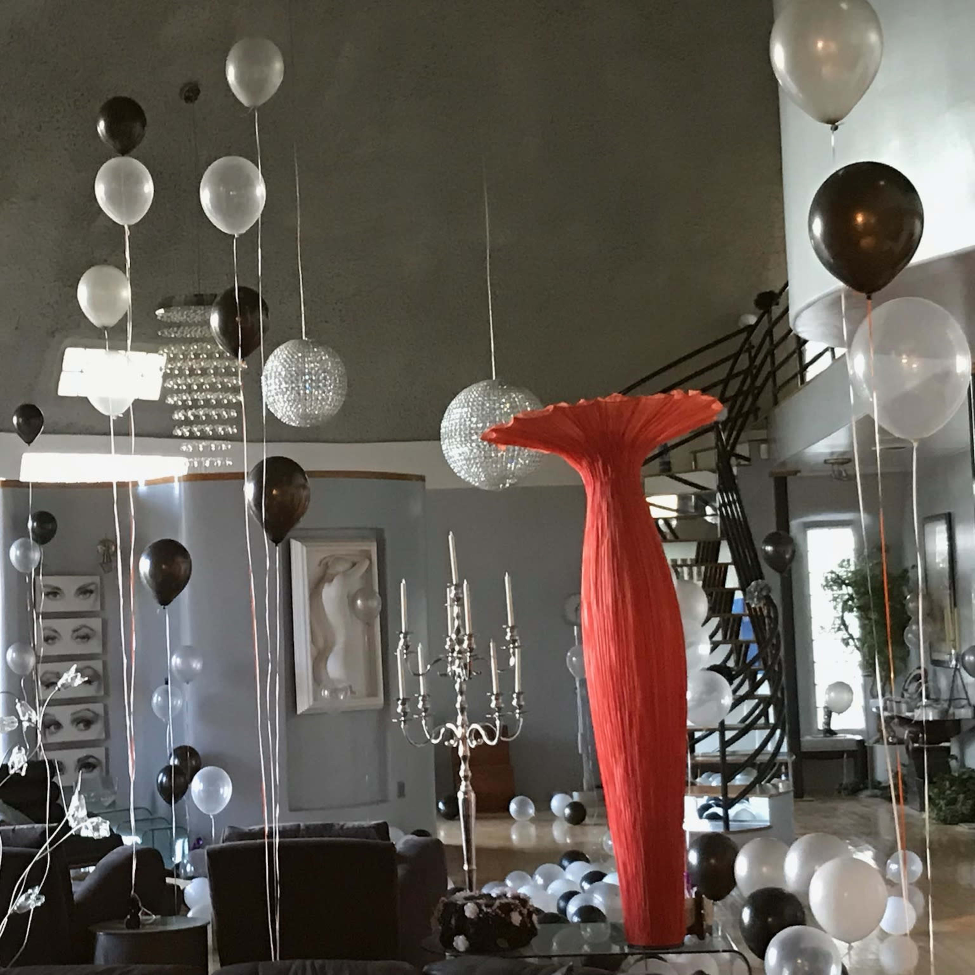 A modern living room decorated with black and white balloons, a red vase, and a chandelier.