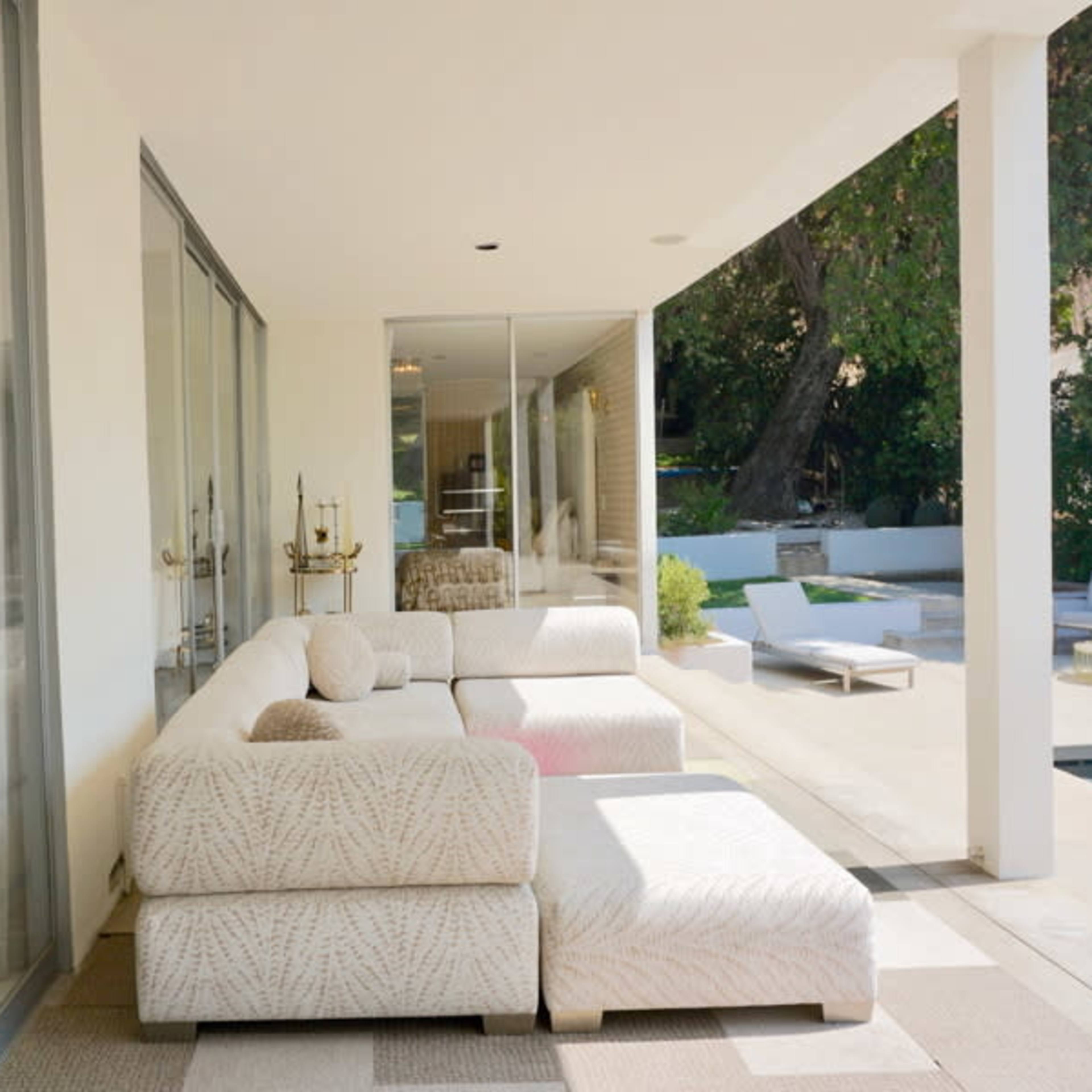 A modern outdoor seating area with a white sectional sofa adjacent to large glass doors leading into a living space.
