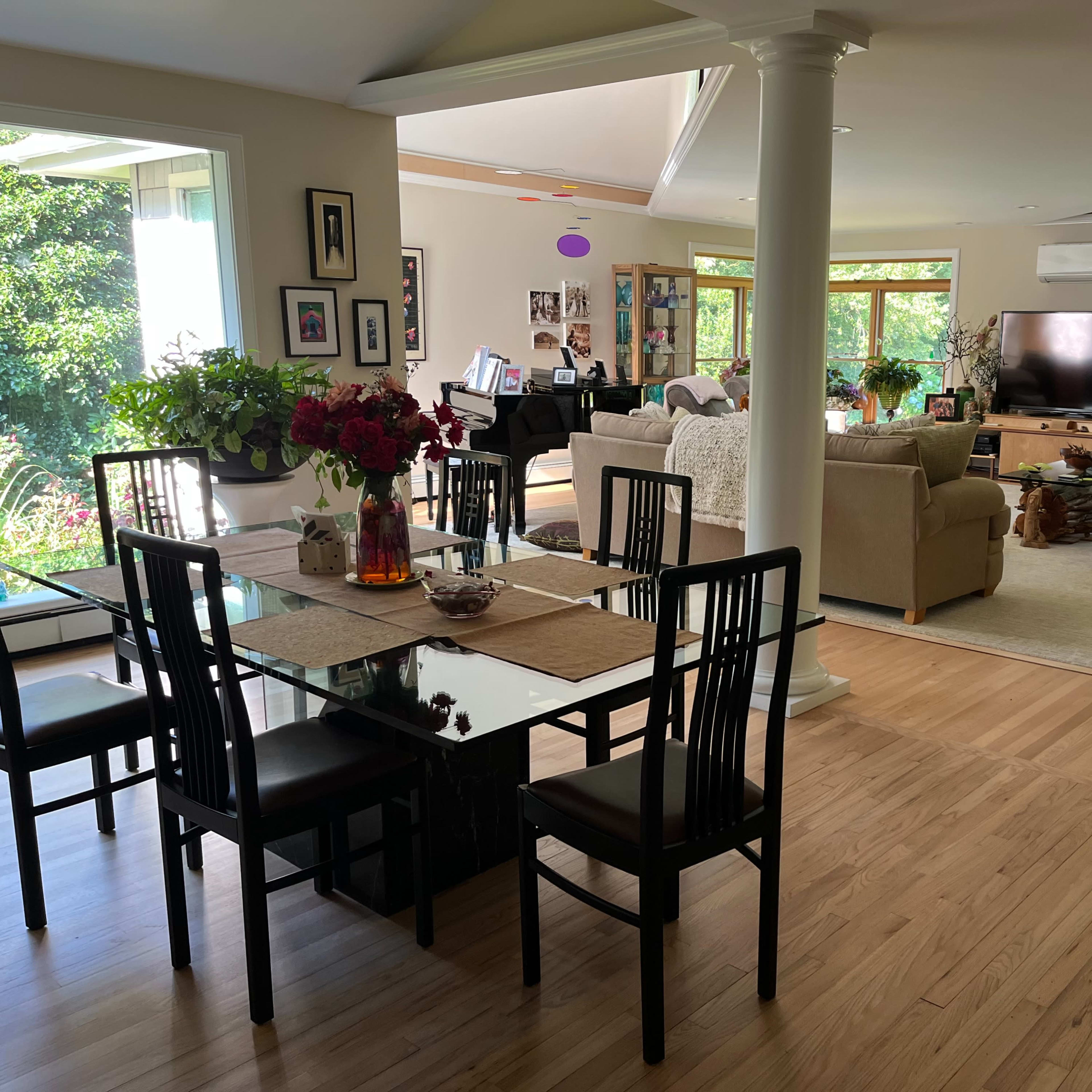 A spacious interior of a home that features a dining area with a glass table and black chairs, leading to a living area with beige sofas and a large television.