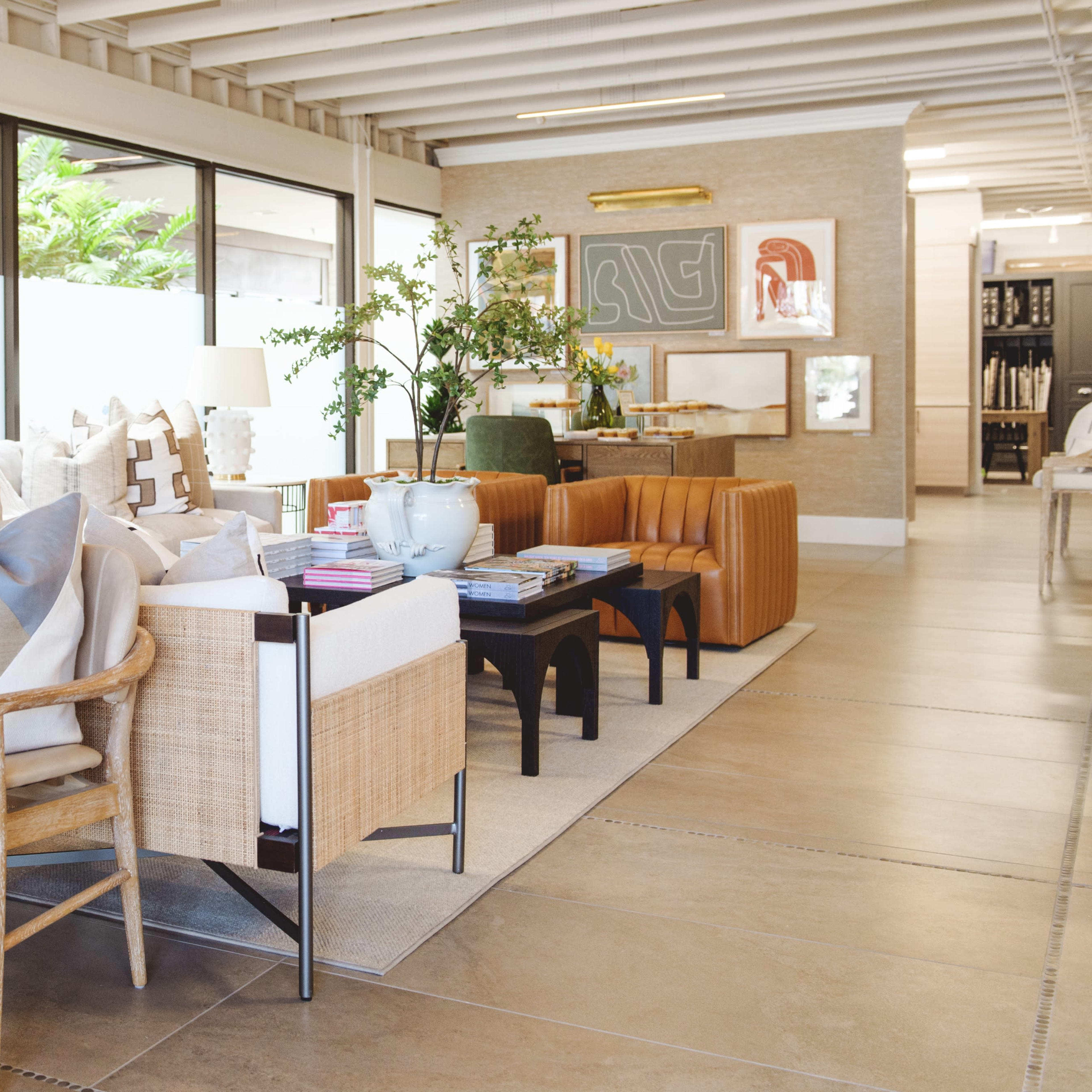 A modern interior space featuring stylish furniture, including a mix of chairs, sofas, and decorative pillows, alongside large windows allowing natural light and greenery to enter.