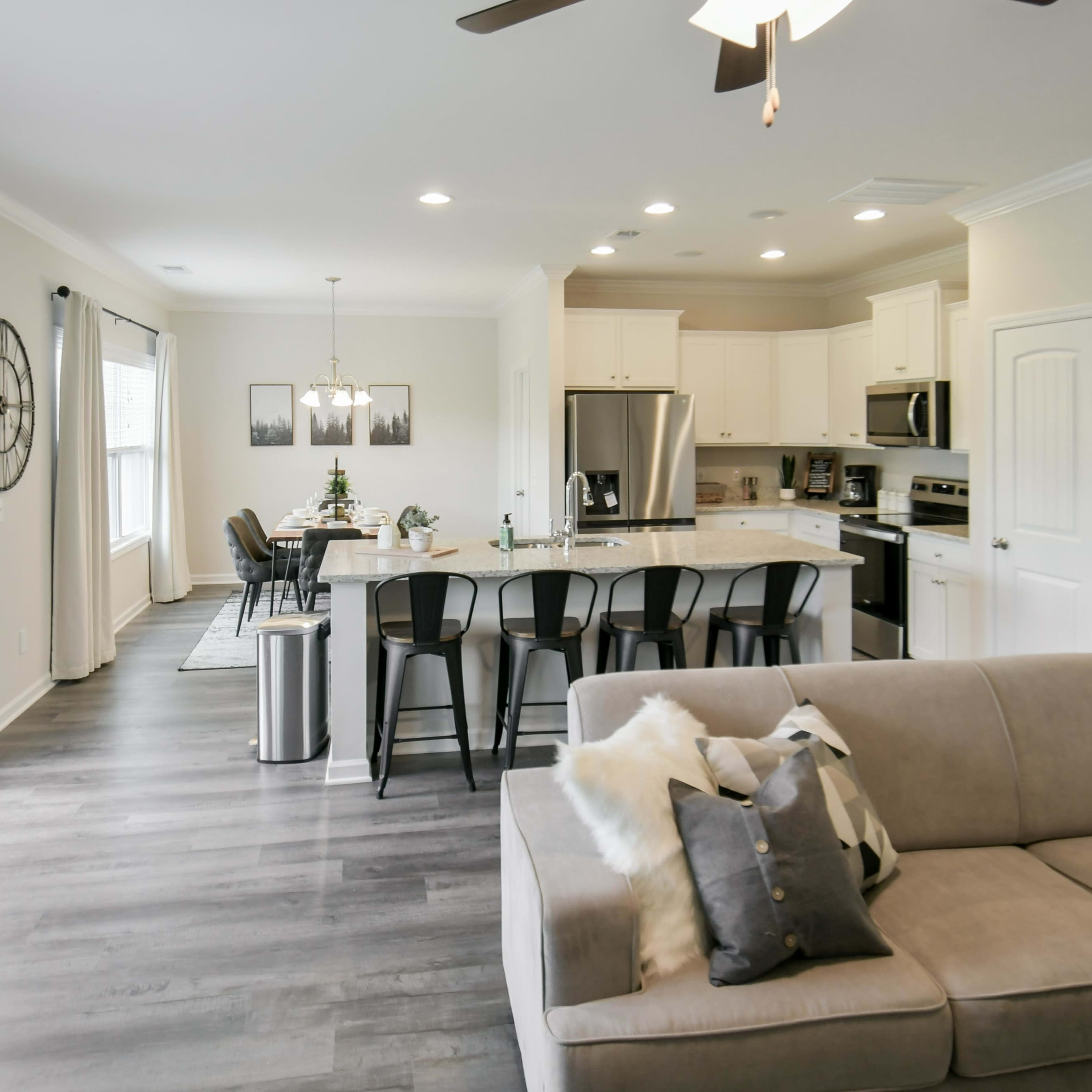 A modern open-concept living space features a kitchen with a large island, dining area, and a cozy seating area with a sofa.