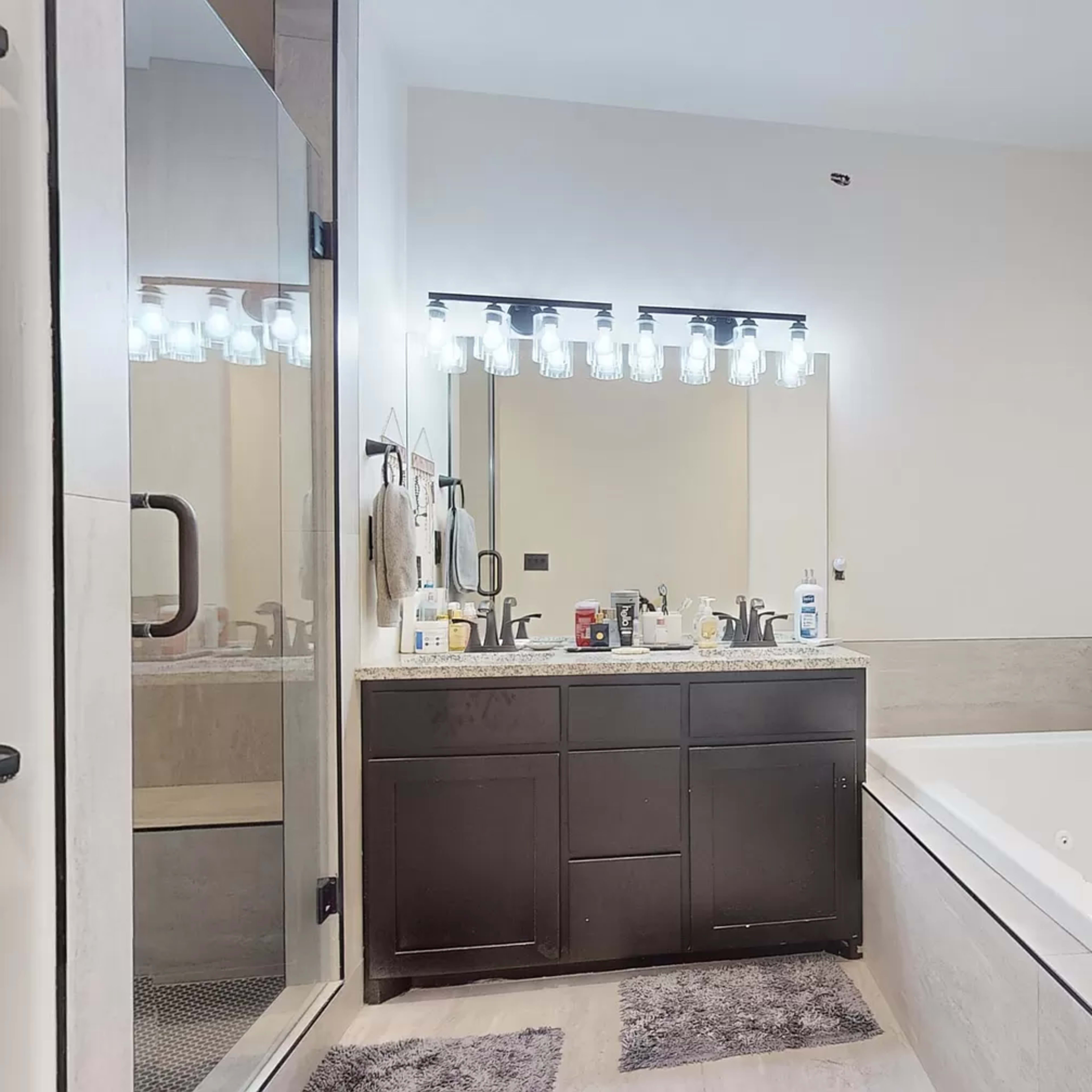 A bathroom featuring a double sink vanity with a mirror above, a bathtub beside it, and a glass shower enclosure.