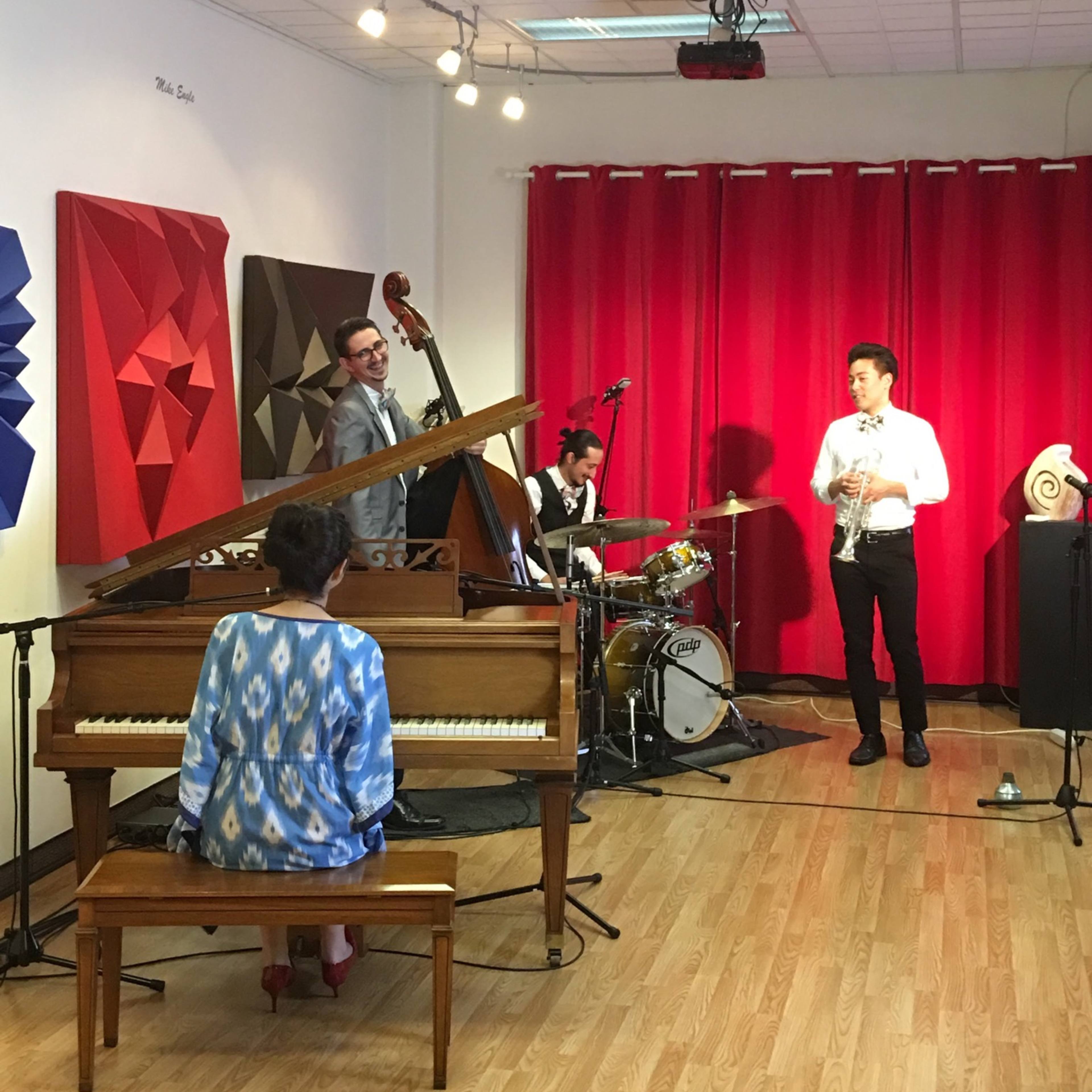 A jazz quartet performs on a small stage in a room with red curtains and abstract wall art.